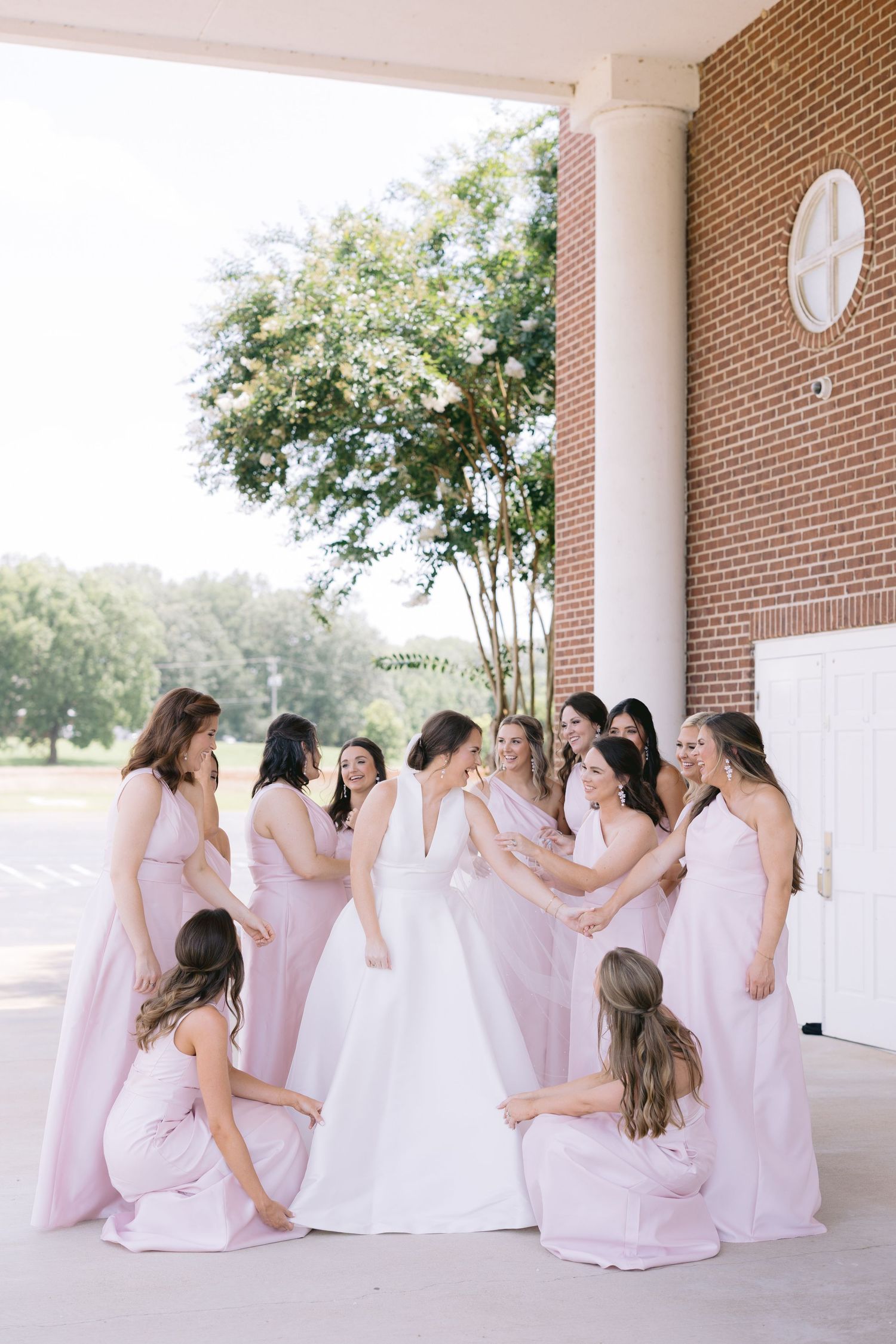 Bridesmaids in pink dresses seated together on portico with white columns.
