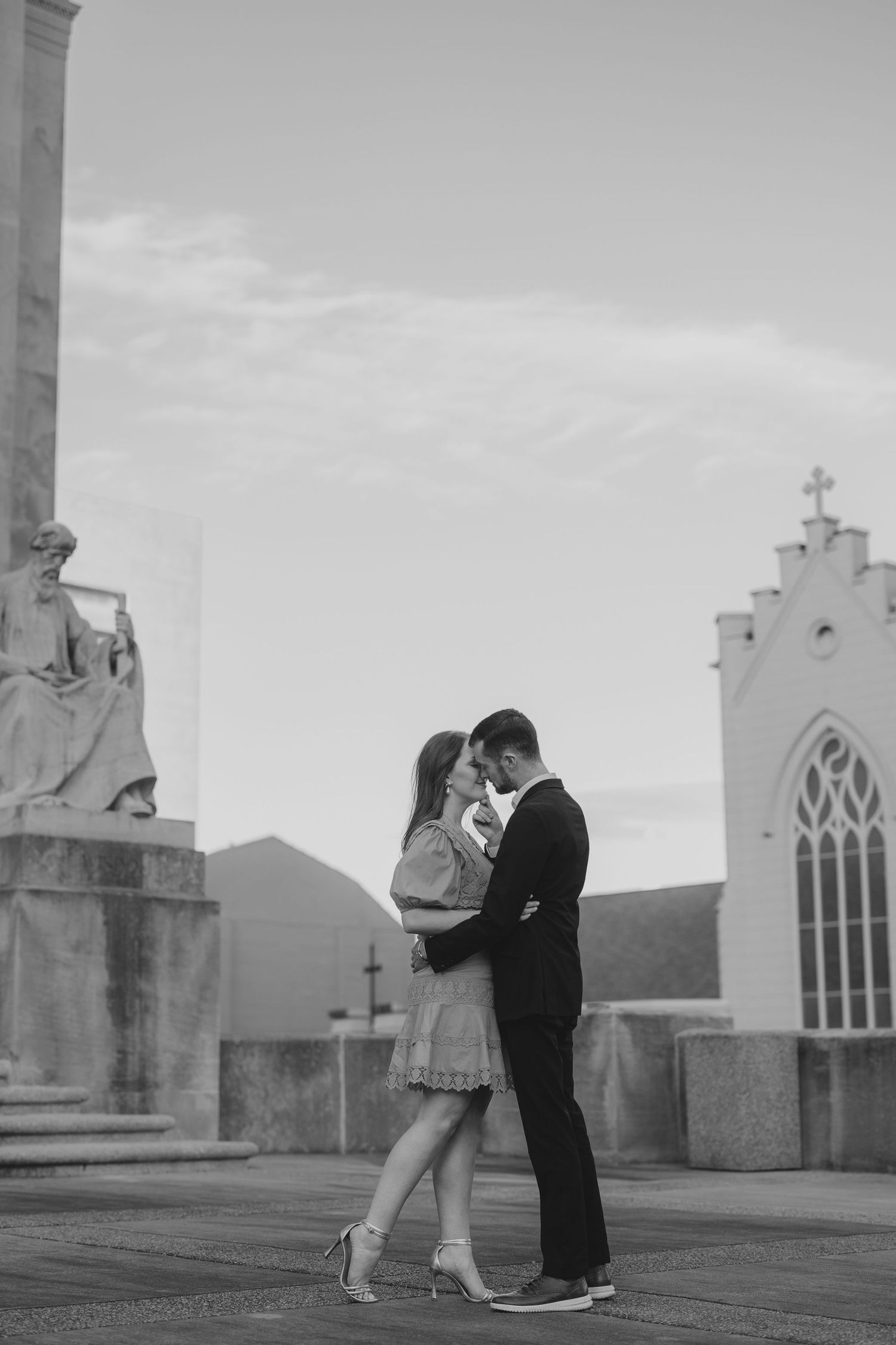 A black and white photo series shows a romantic couple dancing together on a rooftop with church spires in the backdrop.