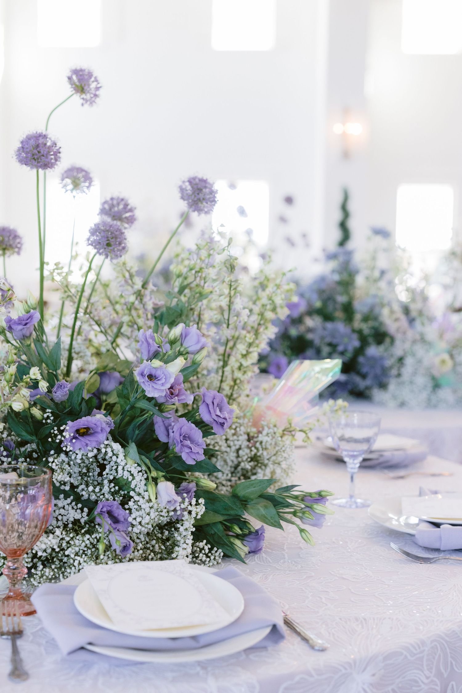 Delicate purple floral centerpieces with baby's breath adorn white reception table settings.