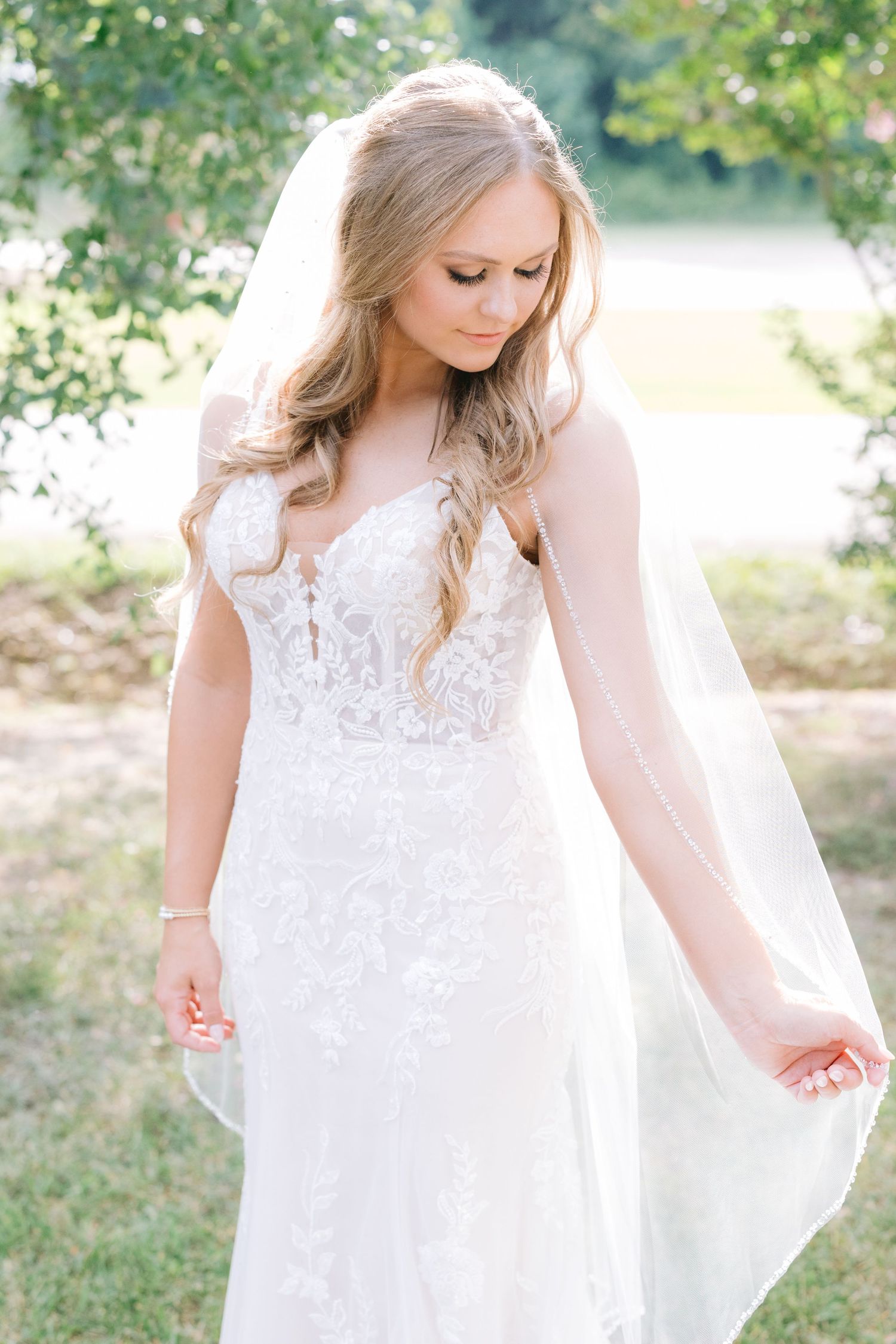 Bride in lace white gown twirls gracefully in outdoor garden setting.