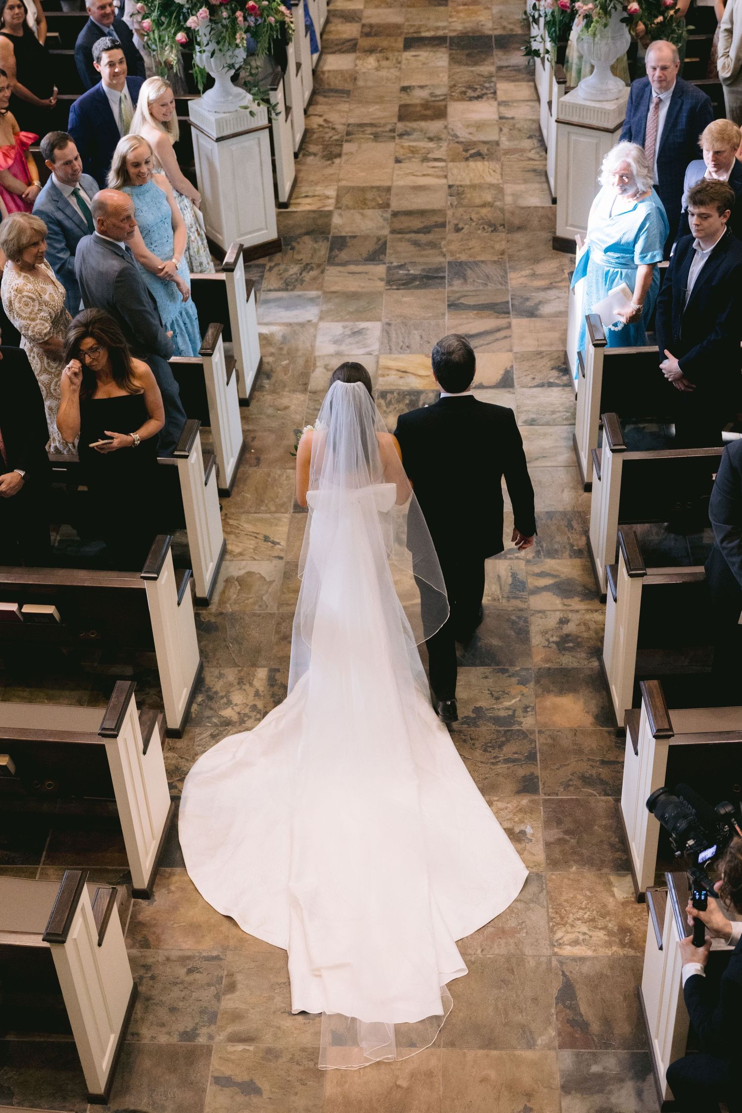 Overhead view of a church wedding ceremony showing a bride walking down the aisle lined with wooden pews.