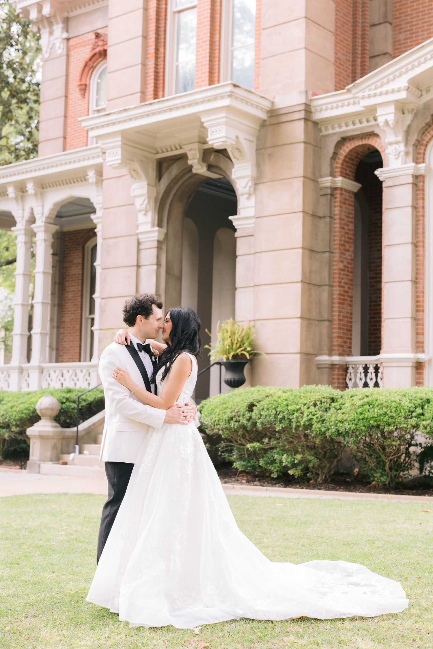 Romantic wedding couple sharing intimate moments in front of a elegant brick mansion with white columns.