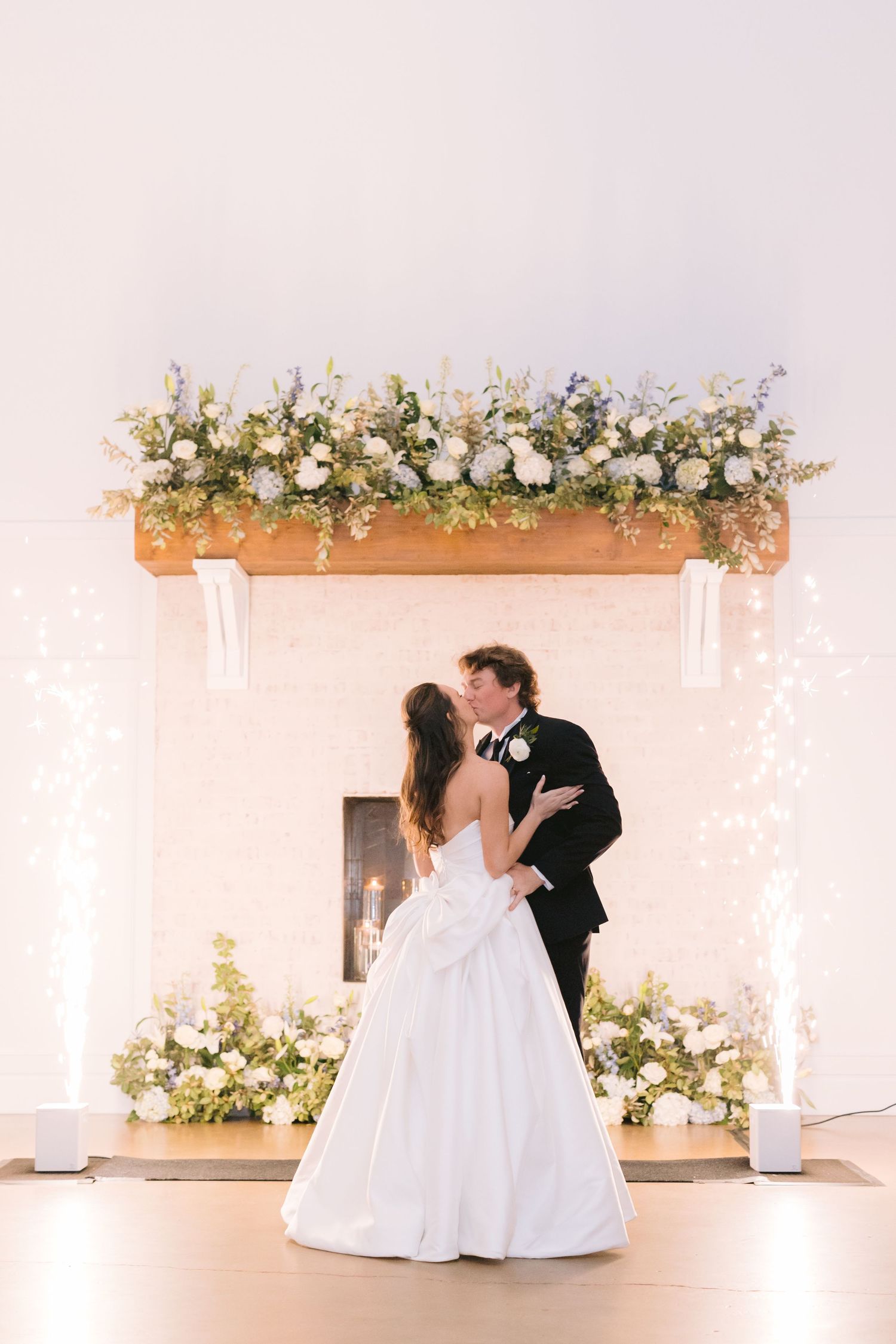 Elegant wedding ceremony under a floral arch with white flowers and soft drapery in a romantic indoor setting.