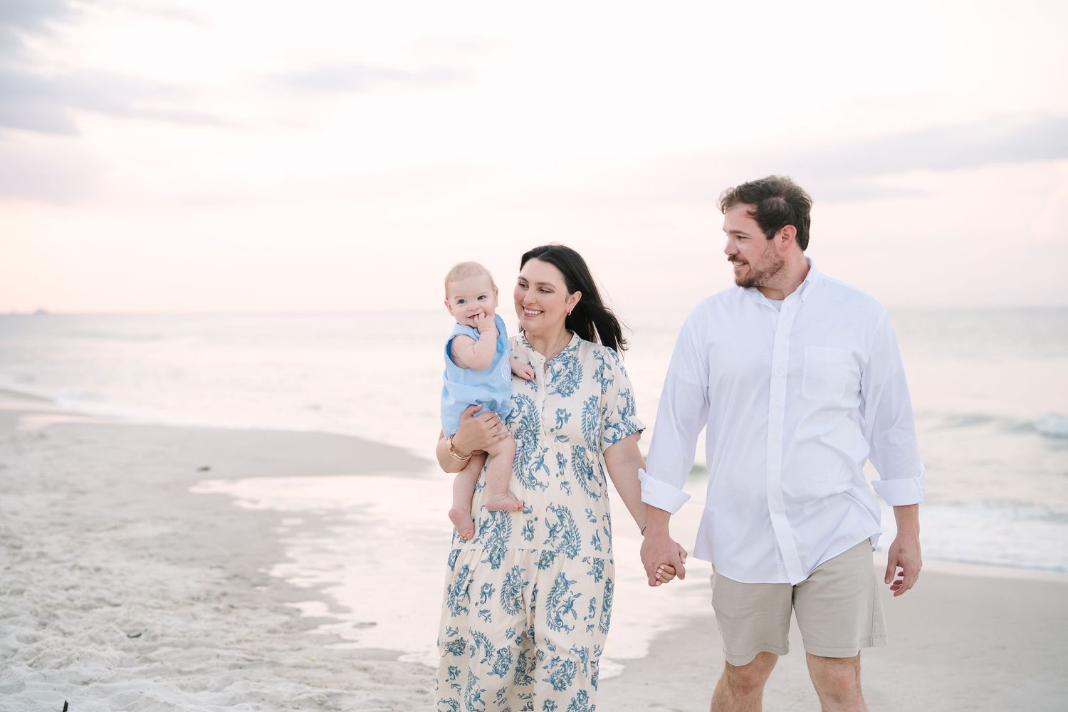 Family walking along a sunny beach wearing coordinated blue and white outfits.
