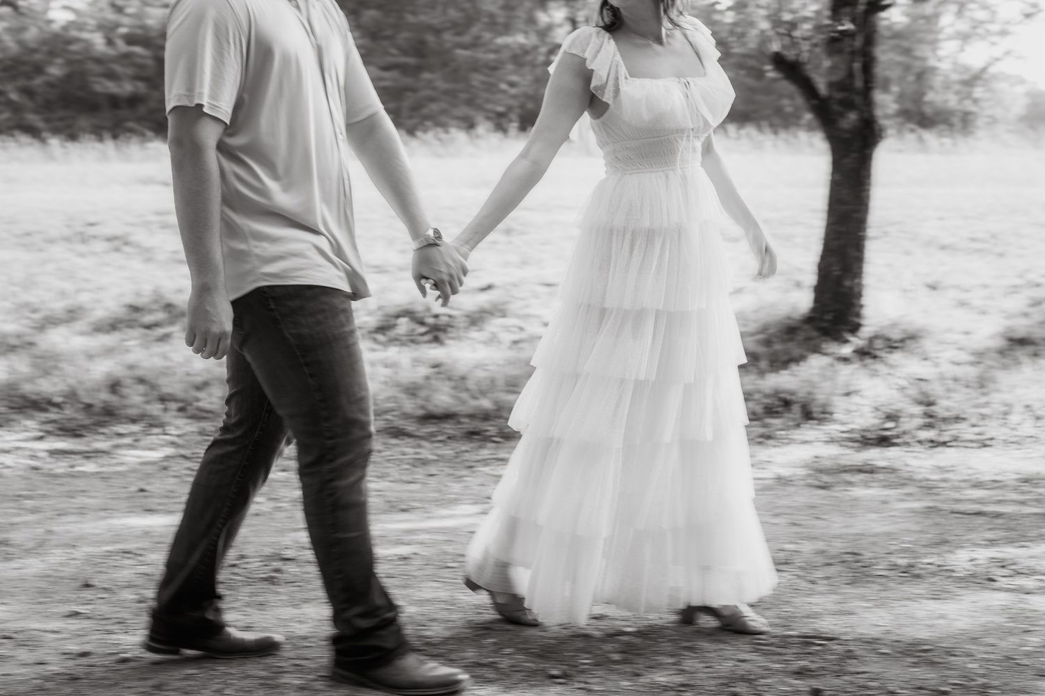 A romantic couple in formal attire holding hands and dancing outdoors in a black and white photograph series.