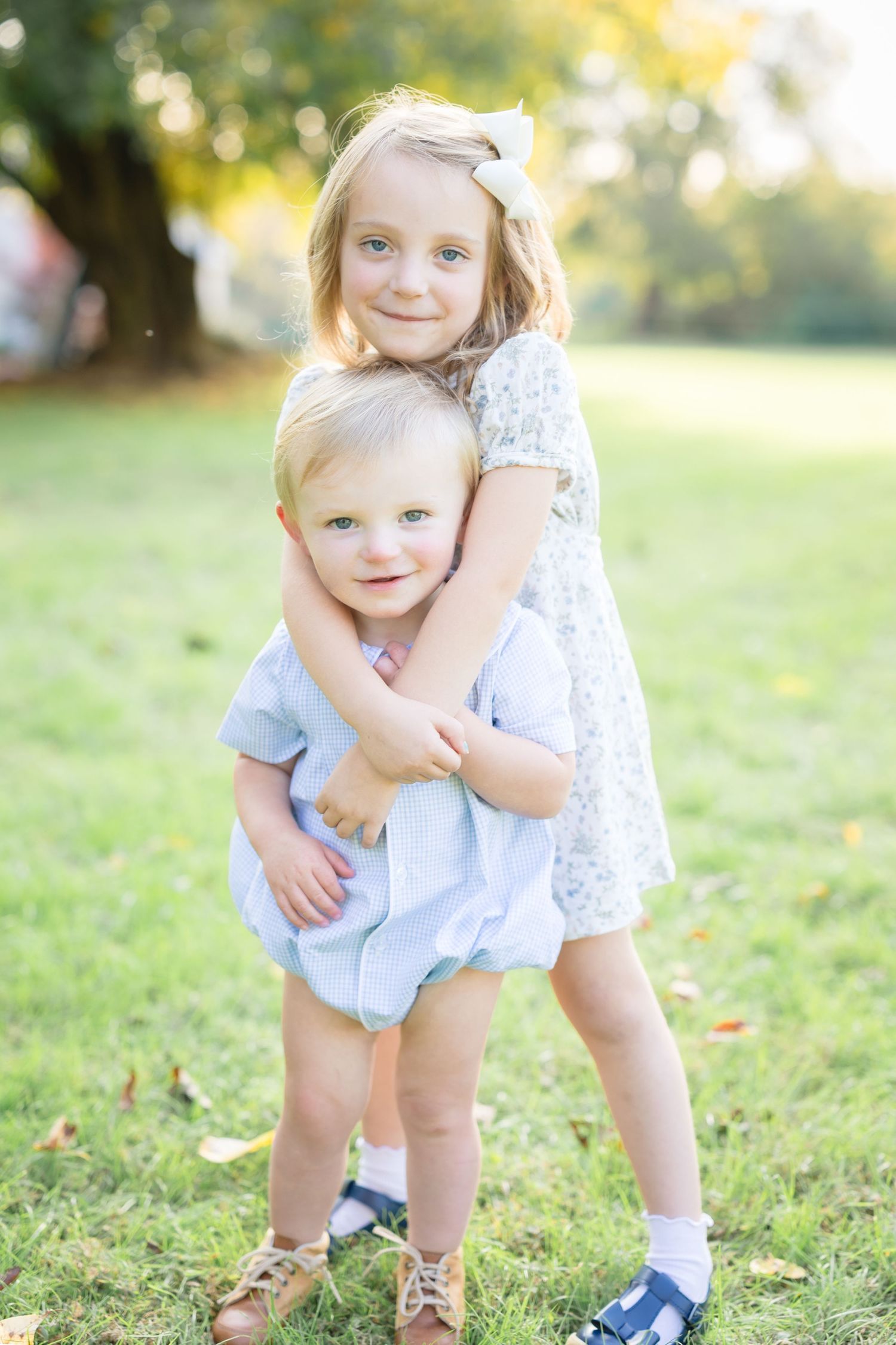 Children play together on grassy lawn during golden hour outdoor photo session.