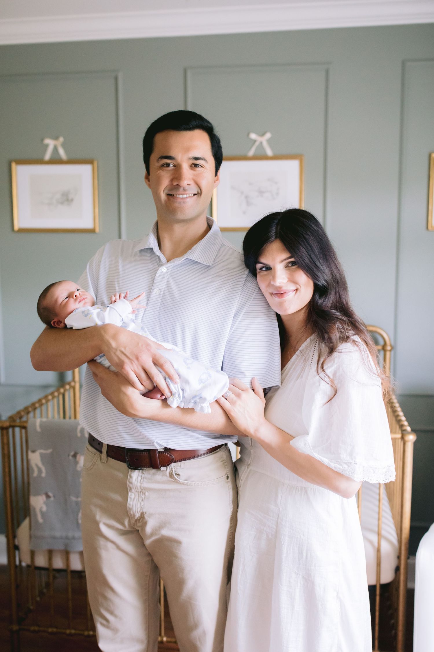 Family photo session in a nursery room with neutral cream and white tones showing parents holding their newborn baby.