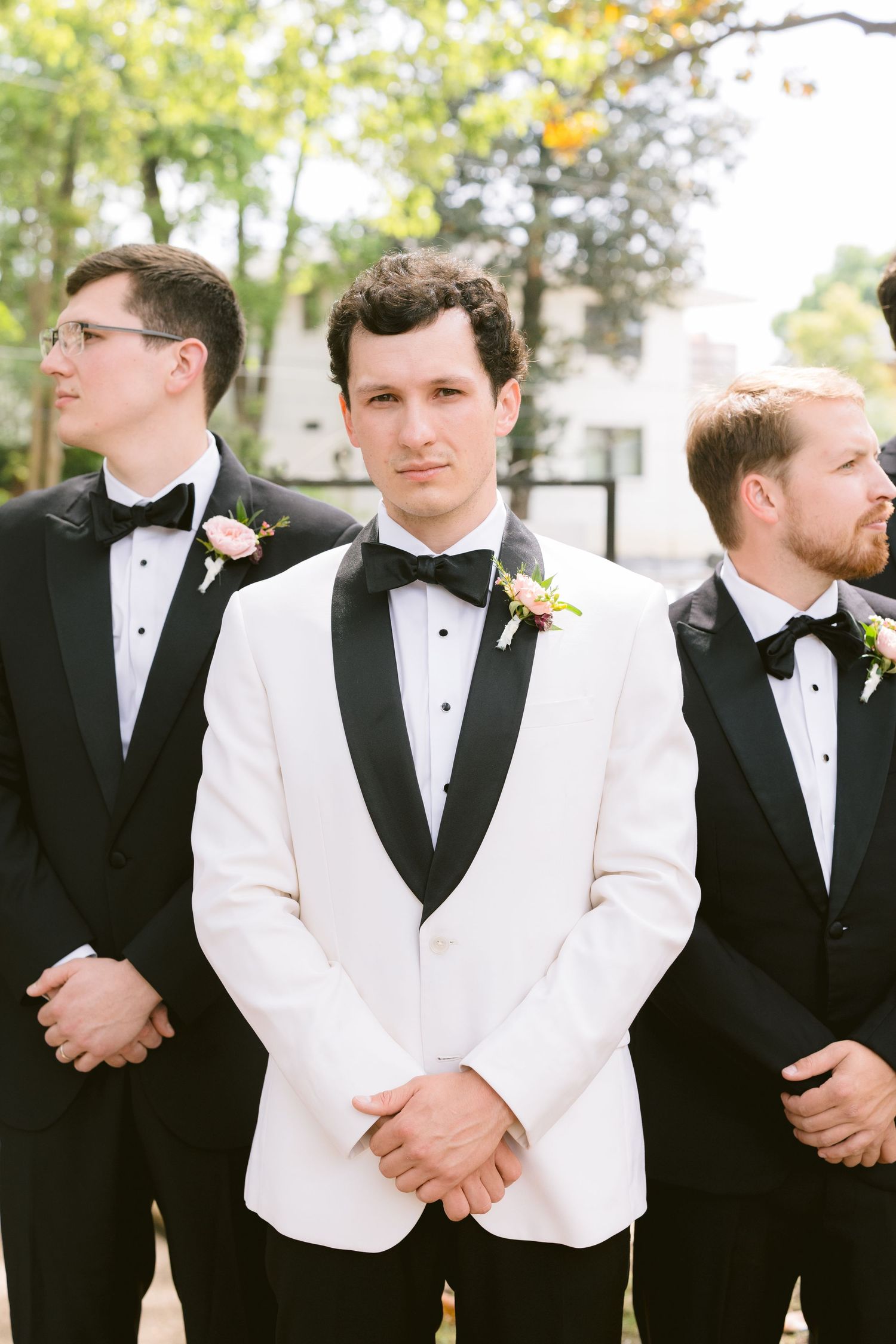 Groomsmen in mixed black and white tuxedos pose outdoors.