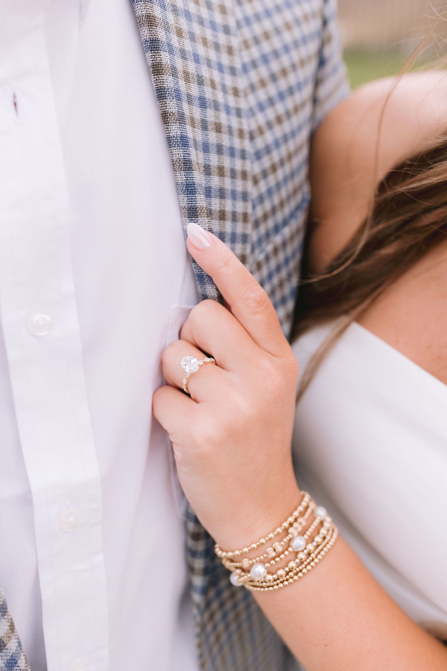 Delicate pearl and gold bangles stacked on a woman's wrist next to soft white and blue checkered fabric.