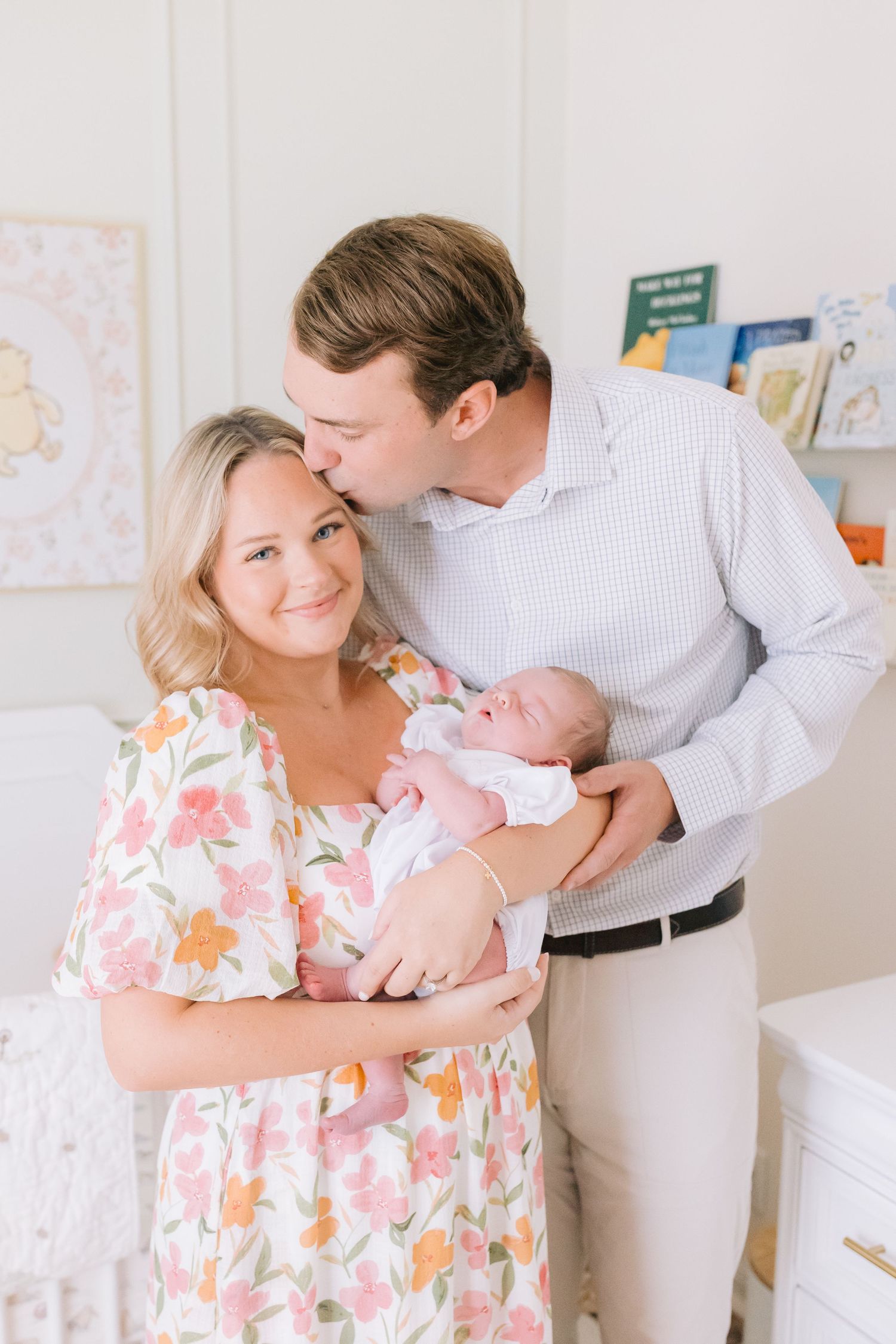 Parents lovingly hold their newborn baby in a nursery decorated with a wall map and floral decor.