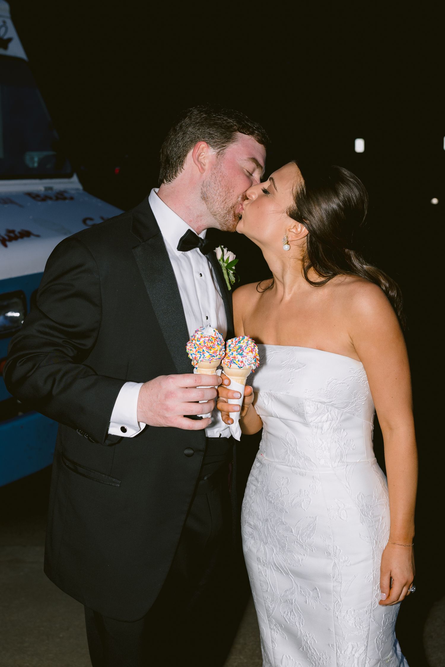 Bride and groom share a kiss while holding waffle cones at their wedding reception.