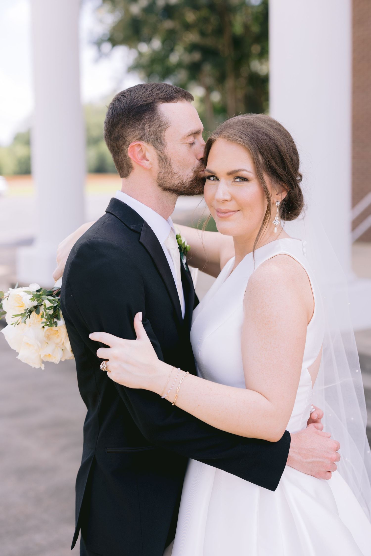 Romantic wedding moment captured under white columns with soft natural lighting.