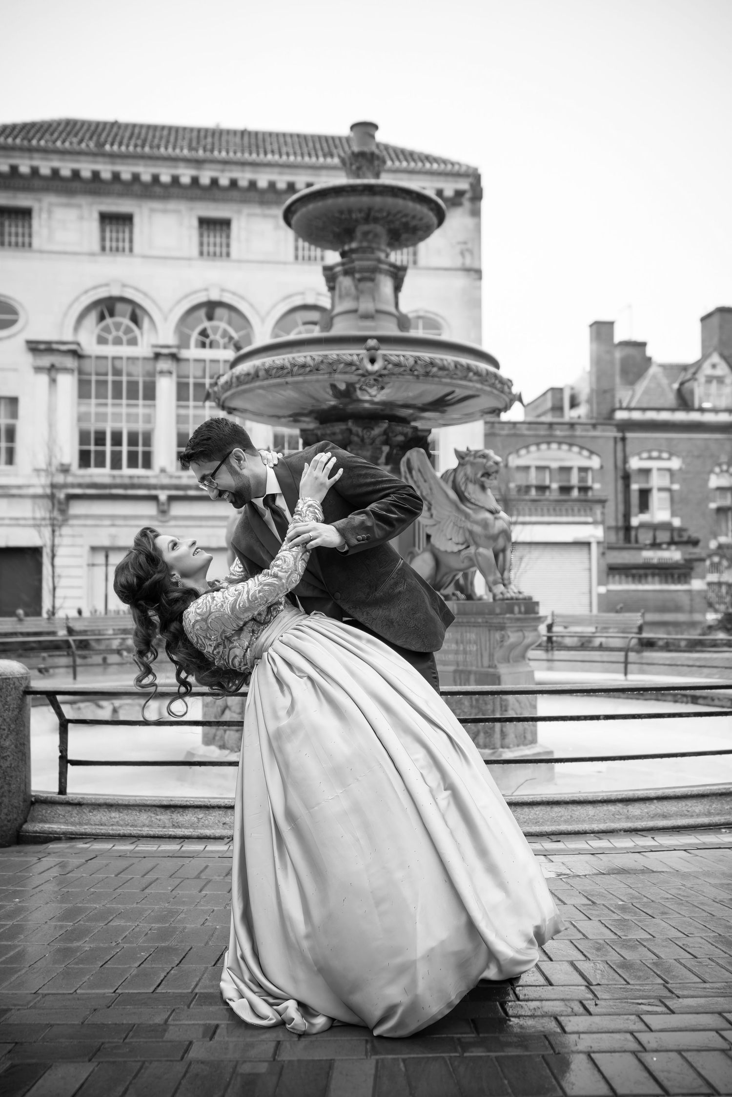 A black and white photo series shows a figure in vintage dress crouching to photograph a fountain at different angles.