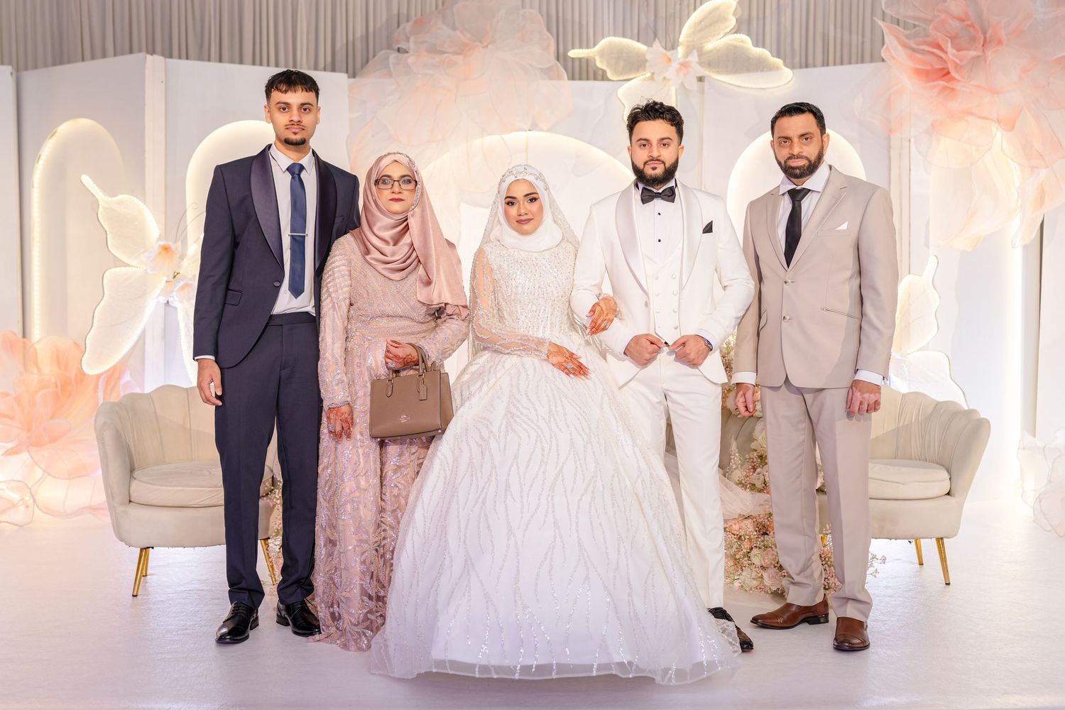 Group standing in elegant white wedding venue with decorative lights and seating.