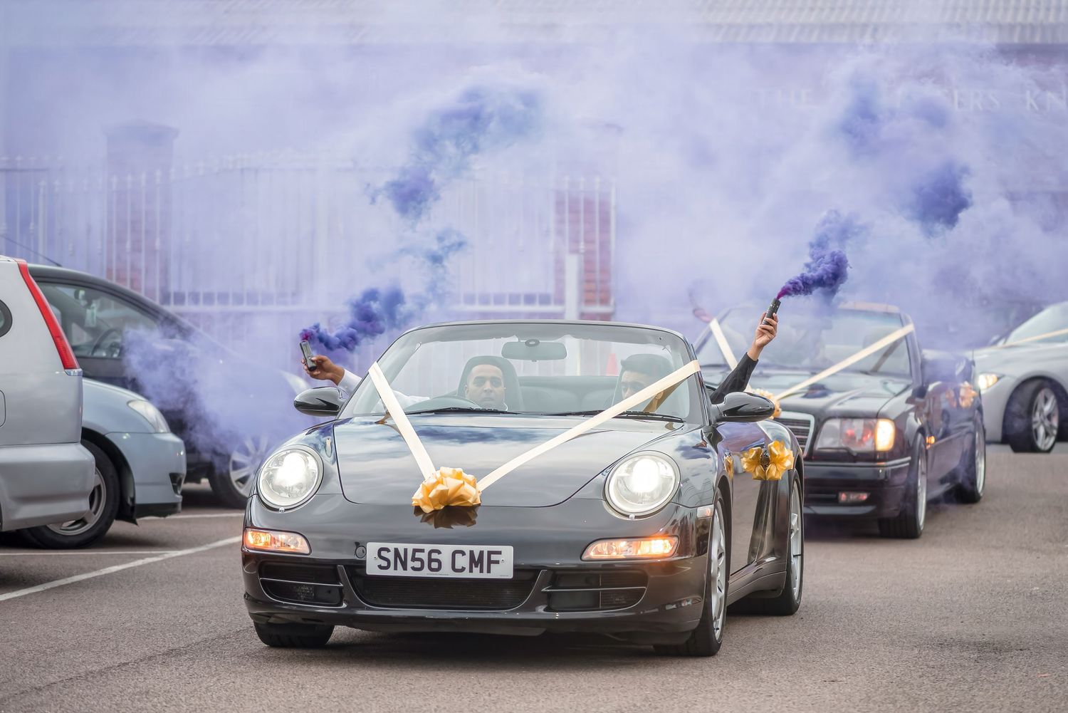 A black Porsche sports car decorated with flags and smoke effects for a celebration.