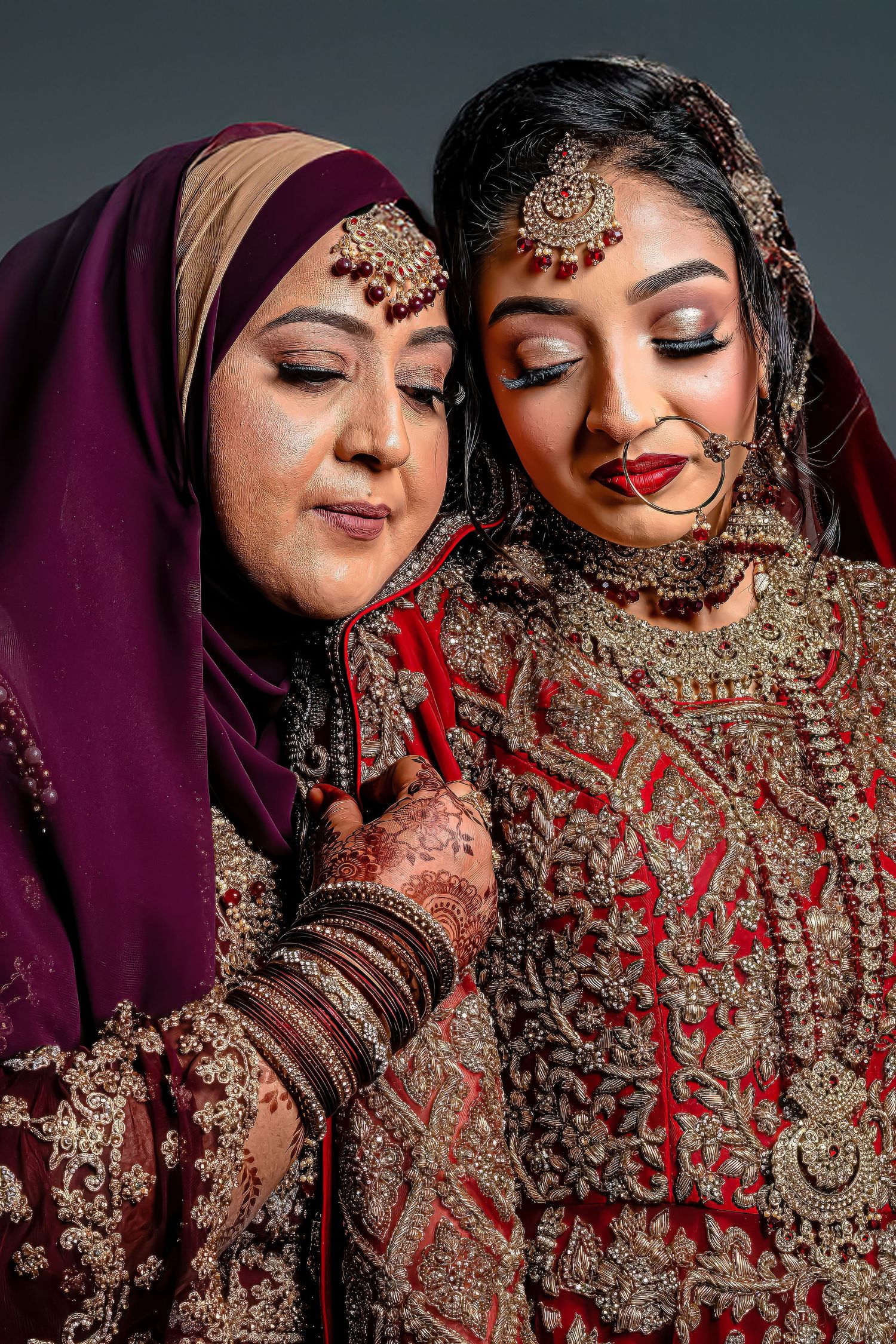Two brides in traditional hijab and embellished outfits share an intimate moment during their wedding.