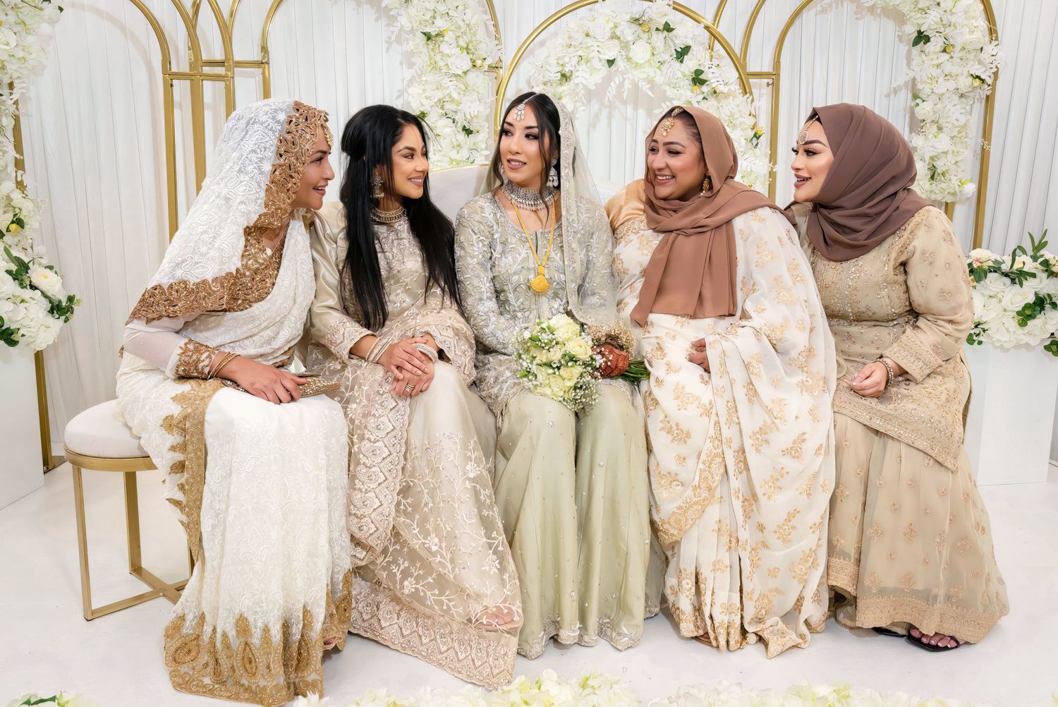 A group in traditional formal attire sitting together on gold chairs at a wedding celebration.