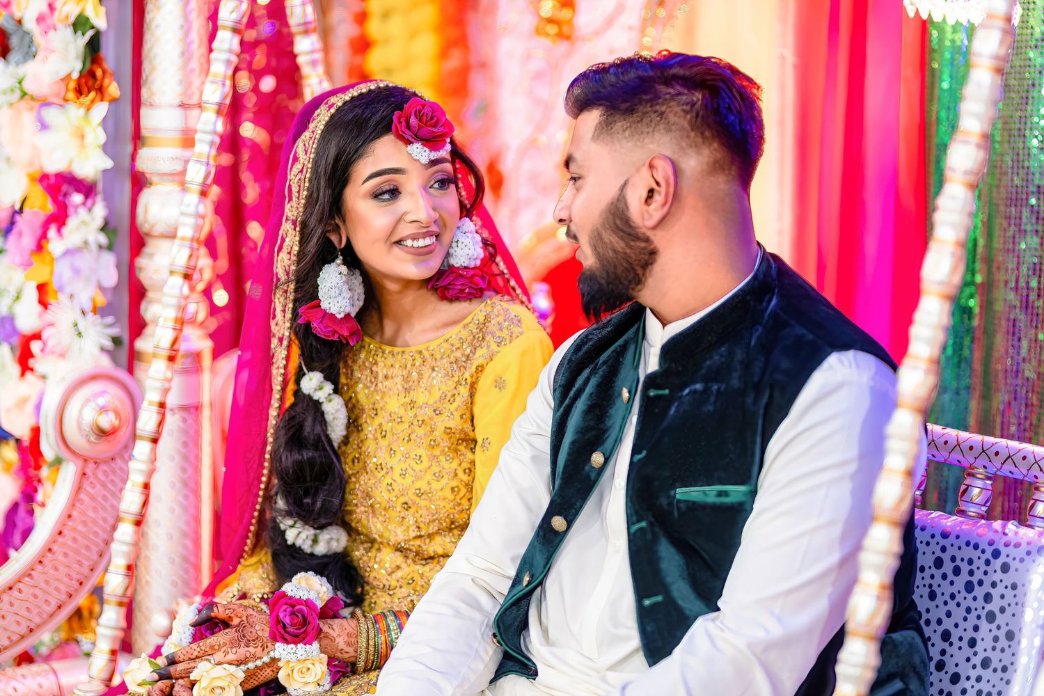 A couple shares a joyful moment at their wedding ceremony against a vibrant backdrop of colorful drapes.