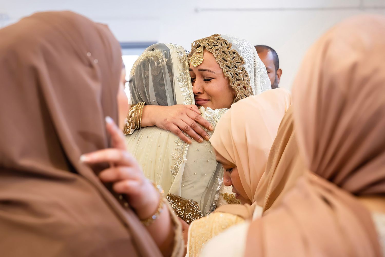 Women in hijabs embrace during an emotional moment at a cultural celebration.
