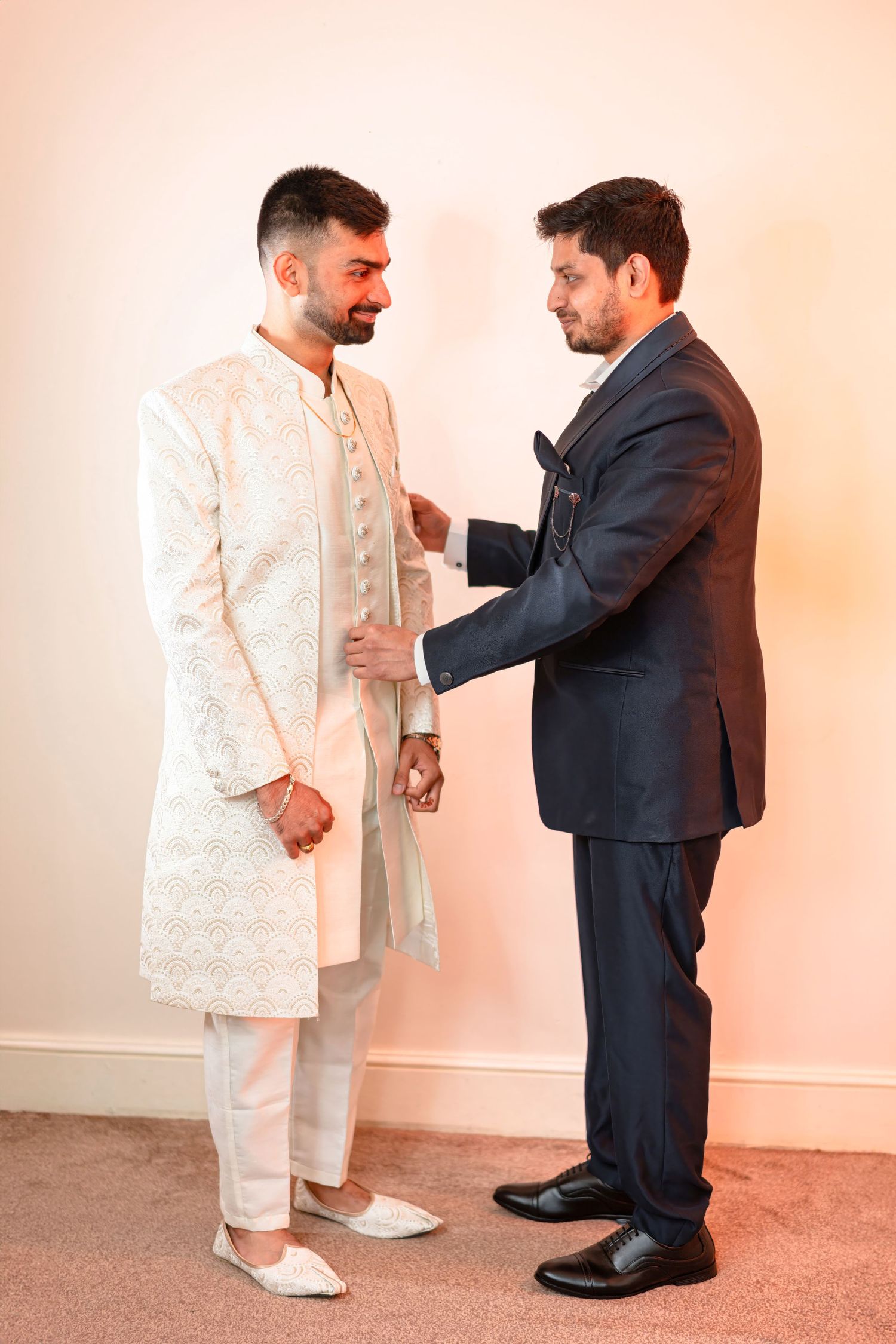 A tender moment between two people, one in traditional white sherwani and another in a navy suit.