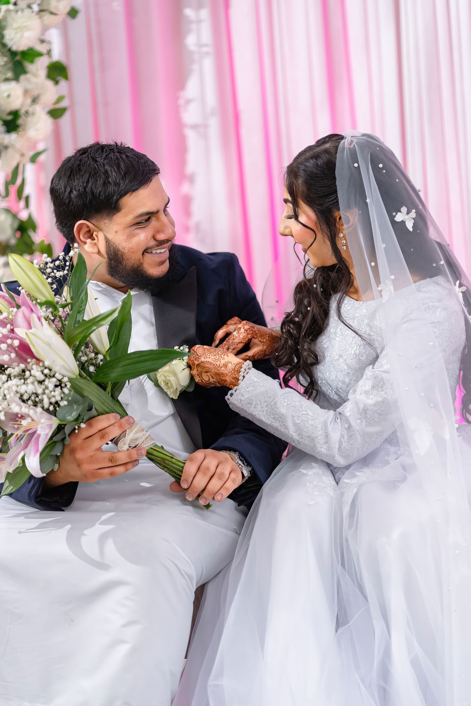 Wedding couple sharing joyful moment with white flowers and pink backdrop.