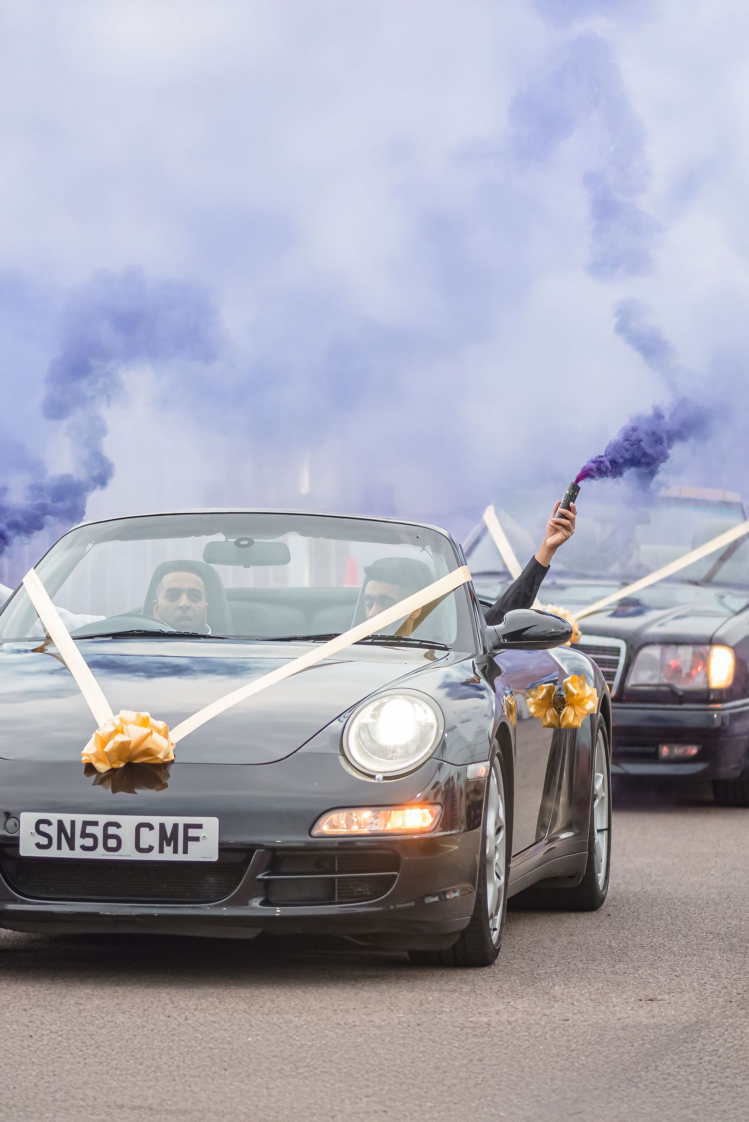 A decorated grey Porsche convertible with smoke flares and white ribbons.