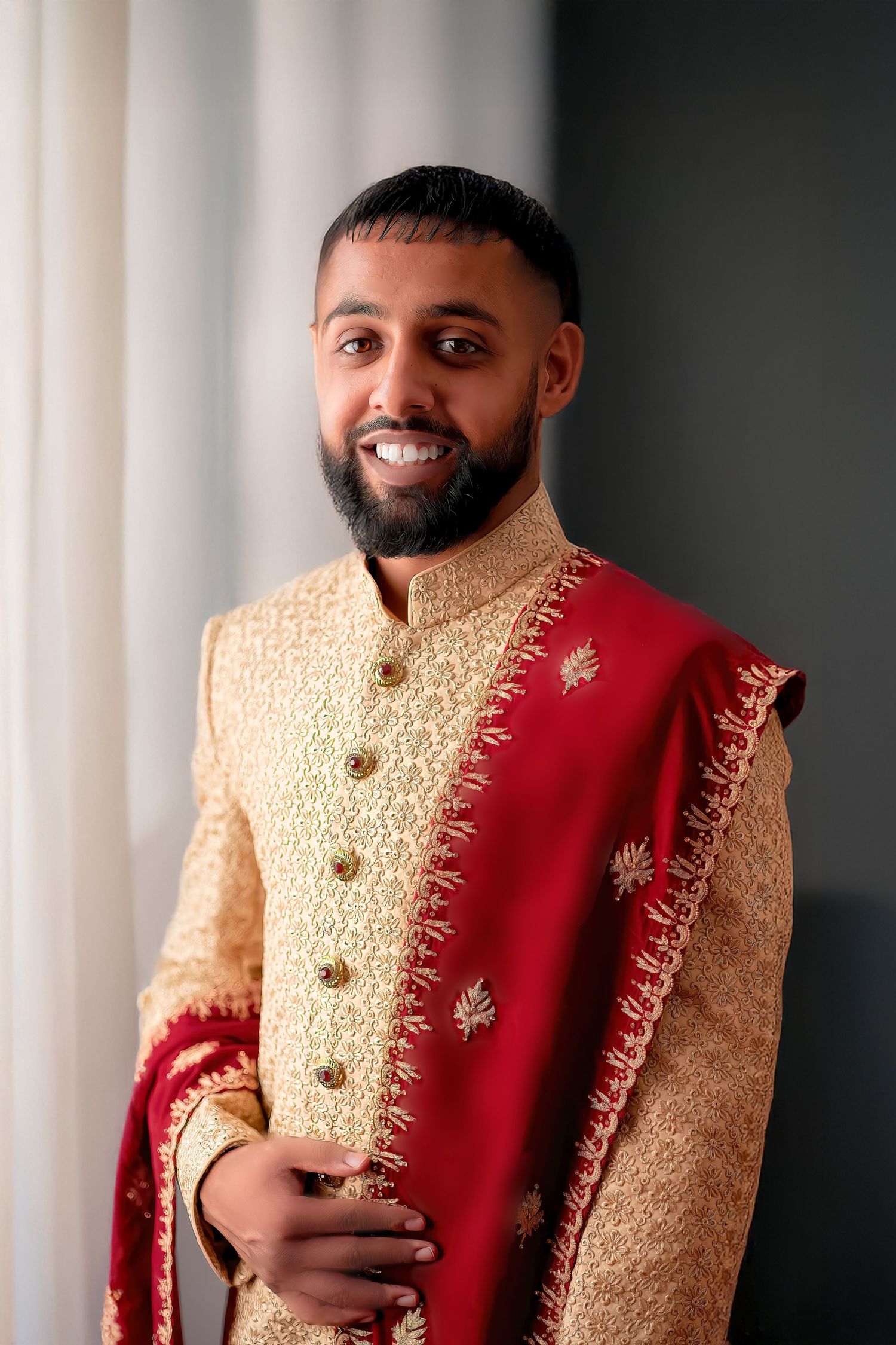 A groom wearing a traditional gold and red sherwani with intricate embroidery.