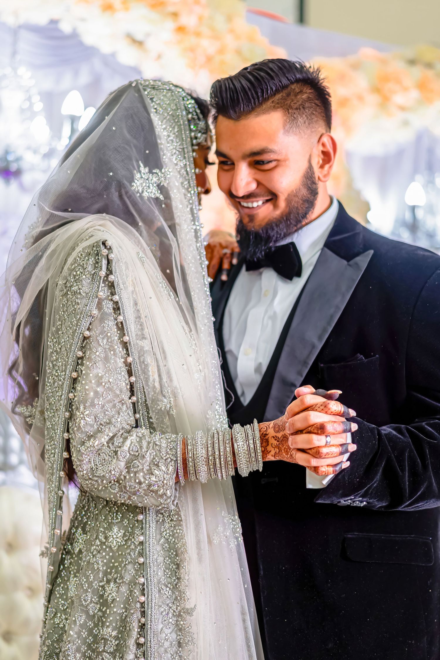 Intimate moment between couple at wedding, with bride in sparkly hijab and groom in classic tuxedo.