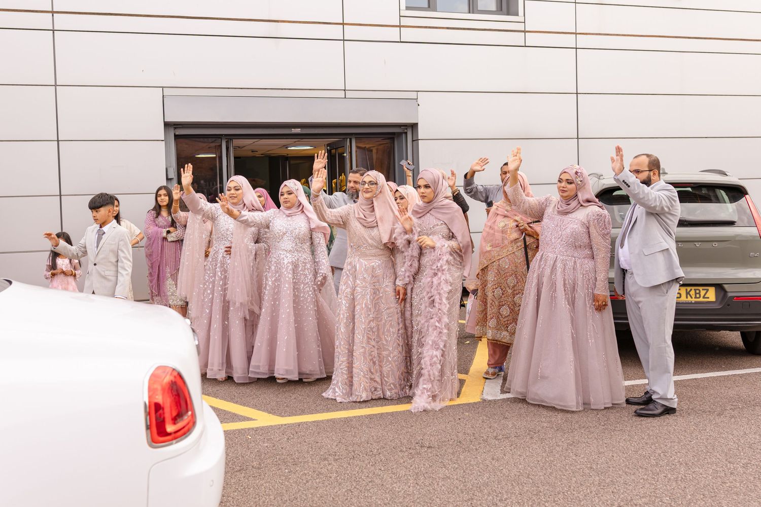 Wedding party in matching mauve and blush formal attire poses together outside building.