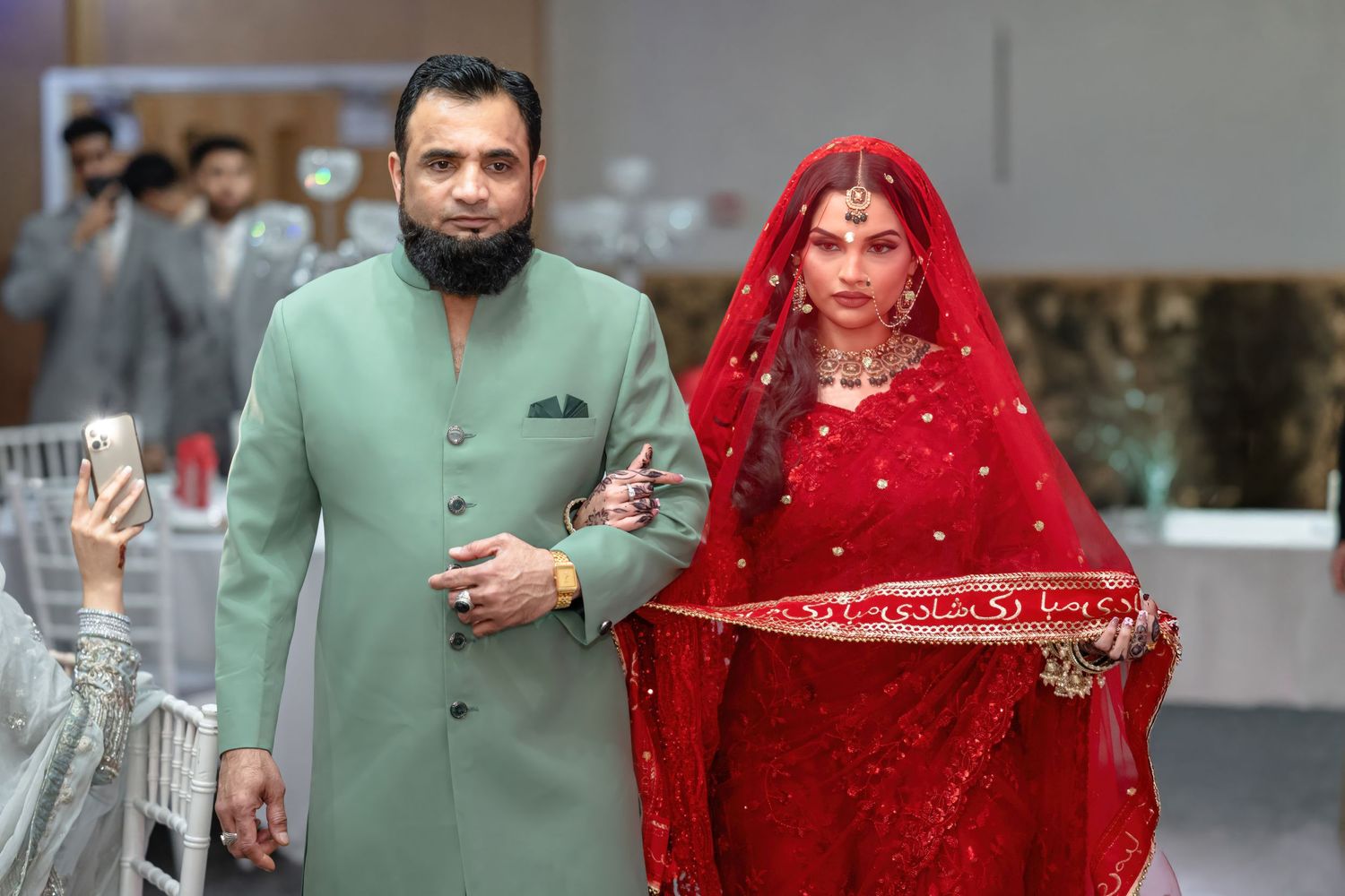 Couple walking together at event, with person in mint green outfit escorting another in red traditional dress.