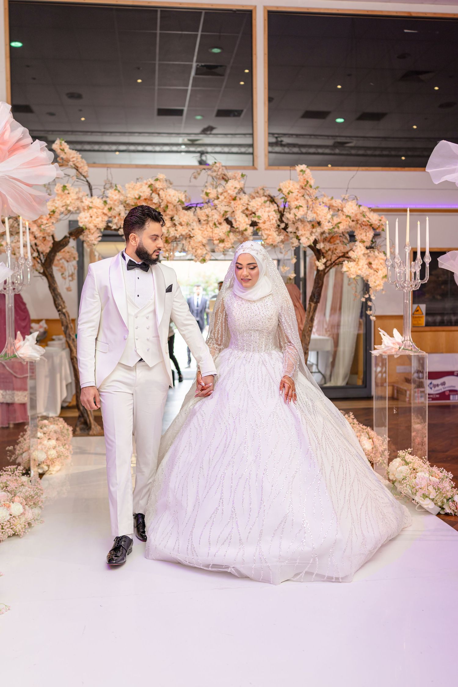 Lavish wedding reception hall decorated with illuminated cherry blossom trees and a white dance floor.