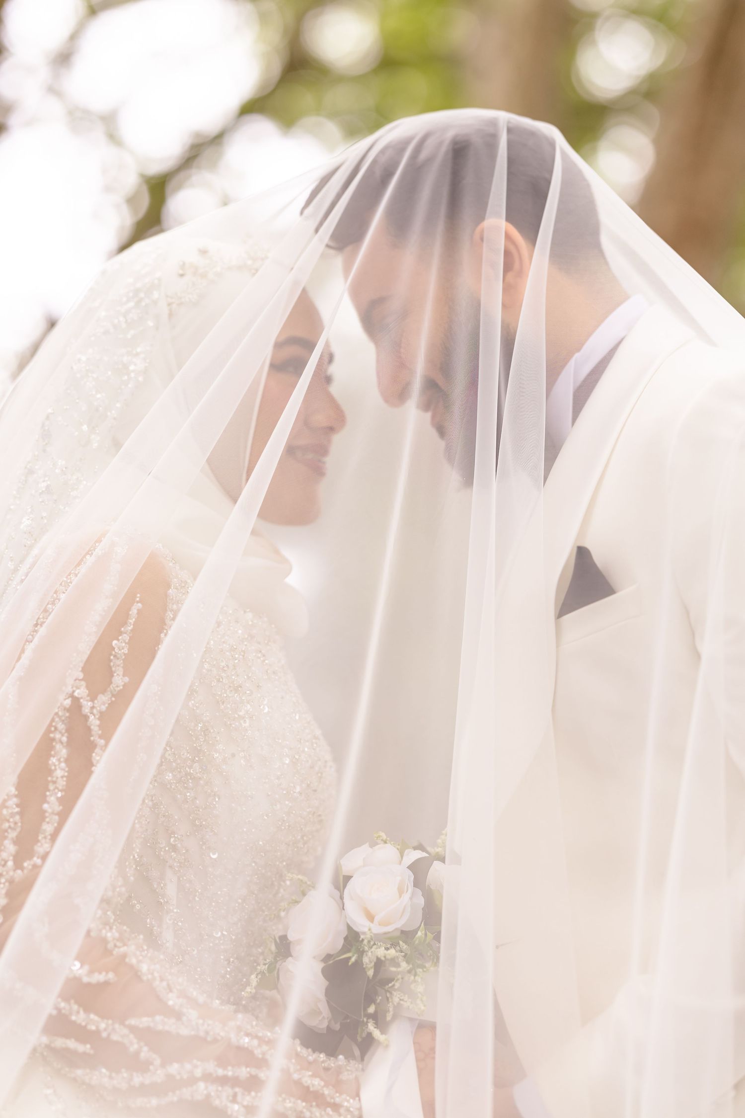 Flowing white wedding veil with delicate lace details captured in natural outdoor lighting.