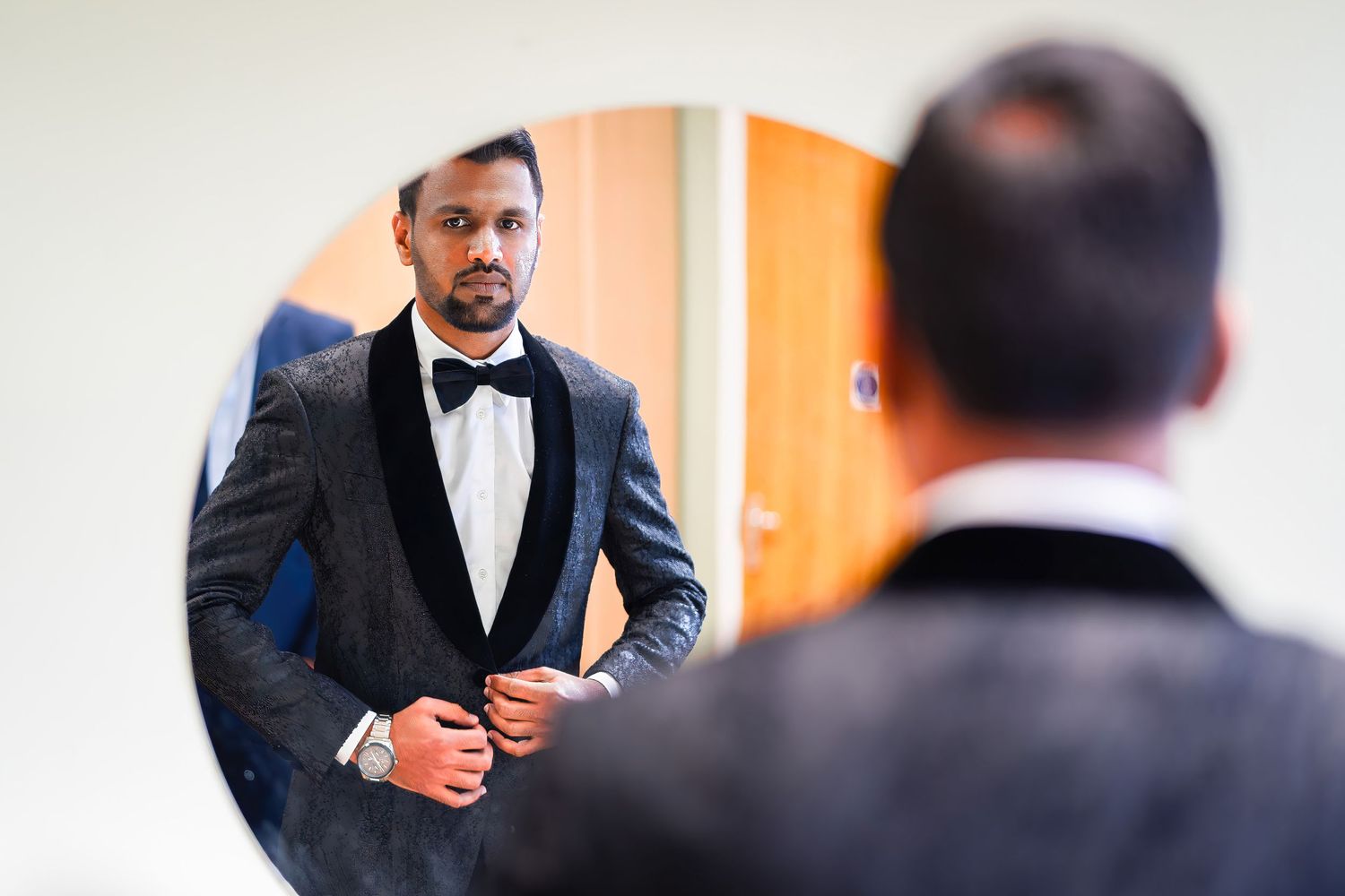 Reflection in mirror shows person adjusting black bow tie while preparing for formal event.
