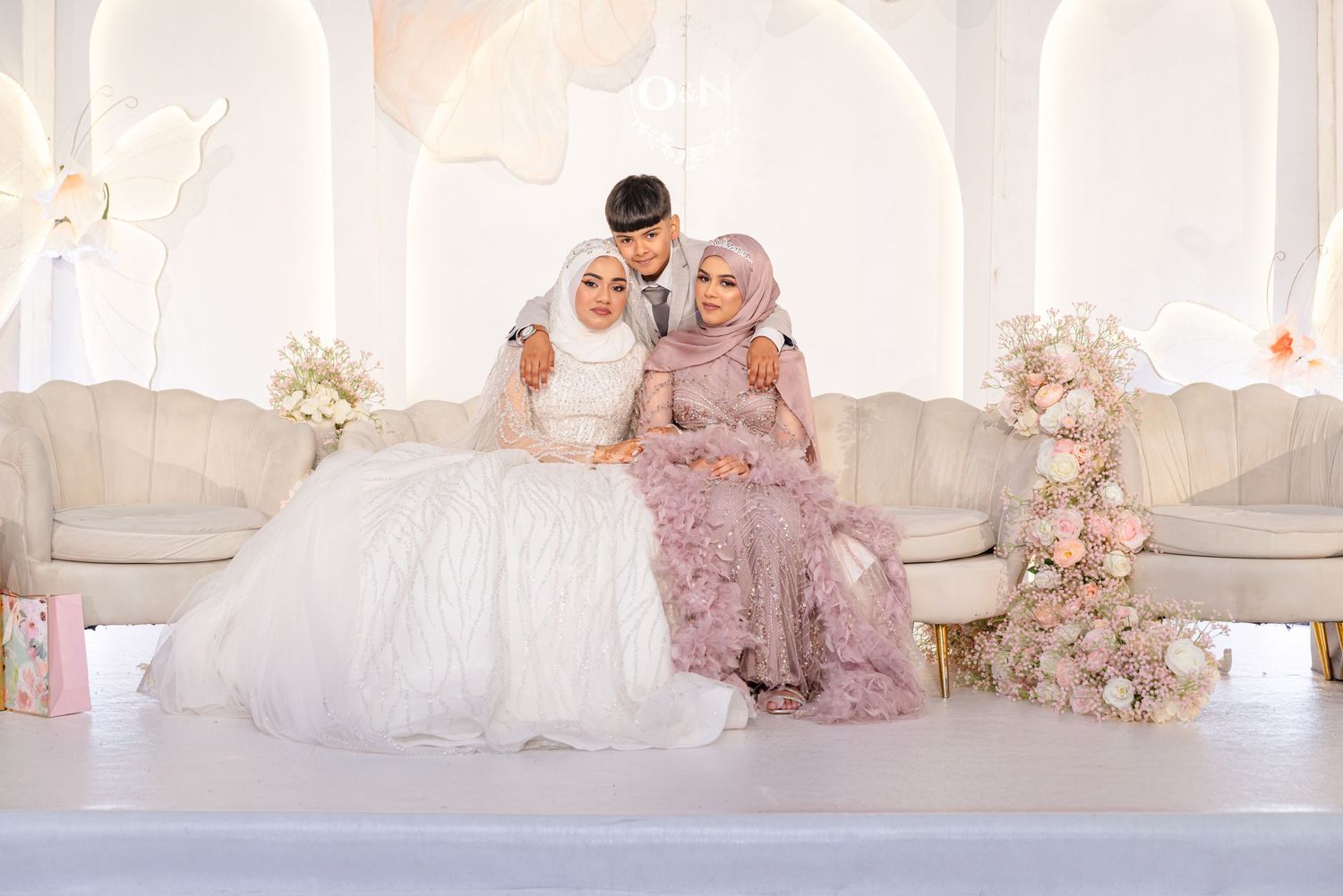An elegant family poses in pink and gold formal attire during a glamorous photoshoot session in a luxurious white room.