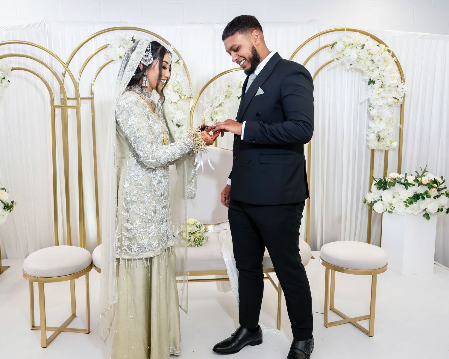 A couple exchanging rings during their wedding ceremony in front of a gold arch backdrop.