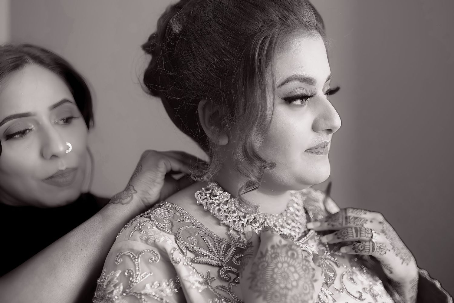 Two people preparing for a formal event with jewelry and elegant attire in black and white.
