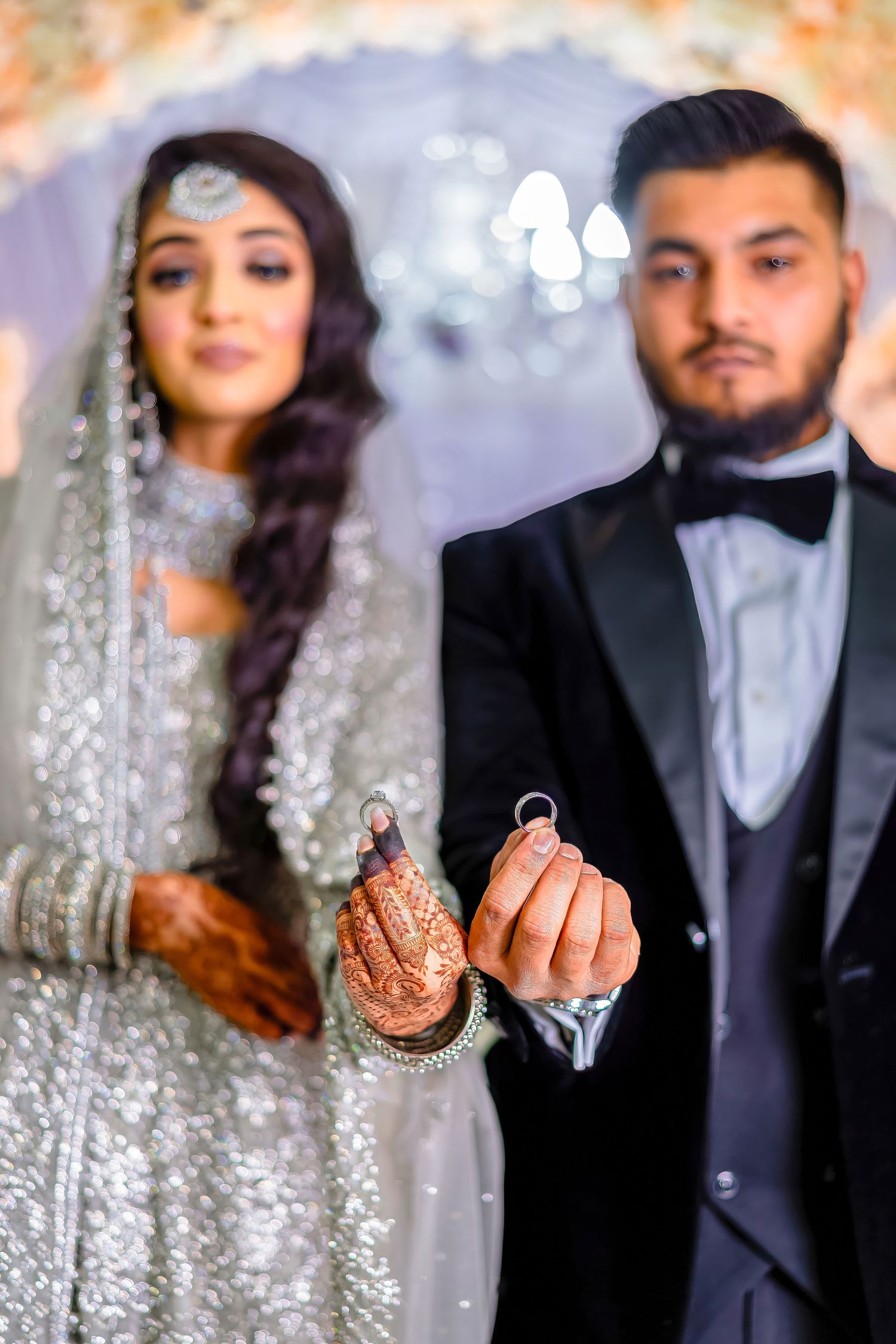 A couple showing their henna-decorated hands while holding rings during their wedding ceremony.