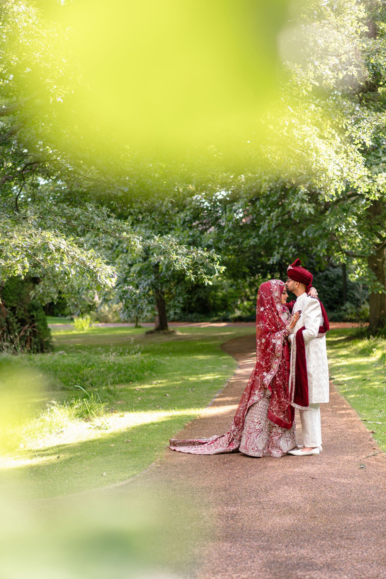 A couple shares a romantic moment on a garden path surrounded by lush greenery and soft sunlight.