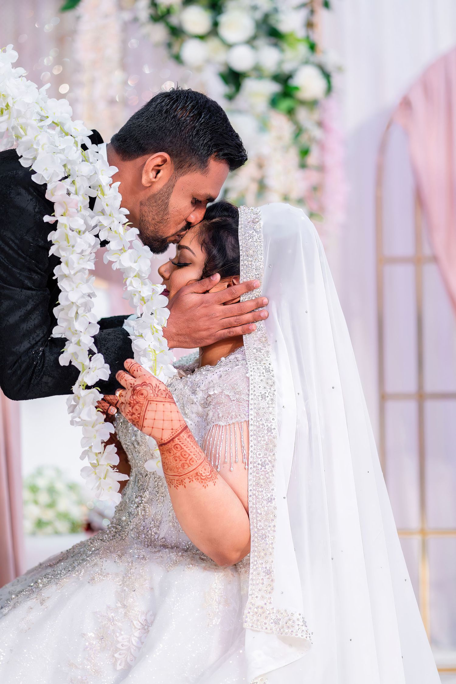 A romantic wedding moment captured as the couple shares an intimate kiss under white floral decorations.