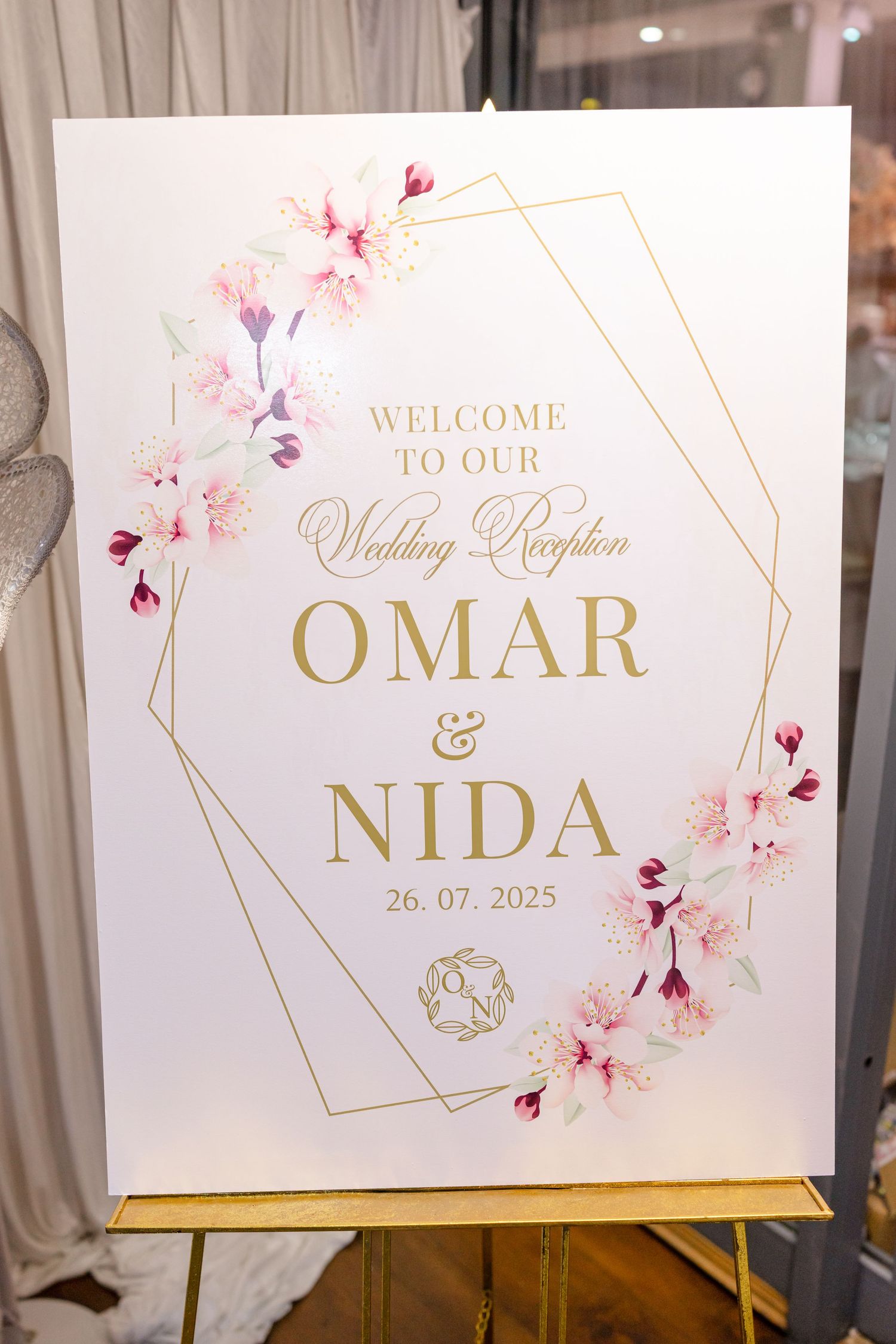 Elegant wedding reception signage with gold text and pink floral design featuring the names Omar and Nida.