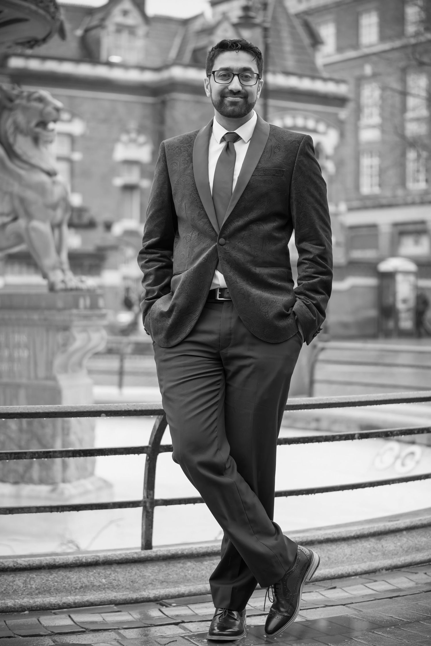 A well-dressed man in a business suit poses confidently against an architectural backdrop.