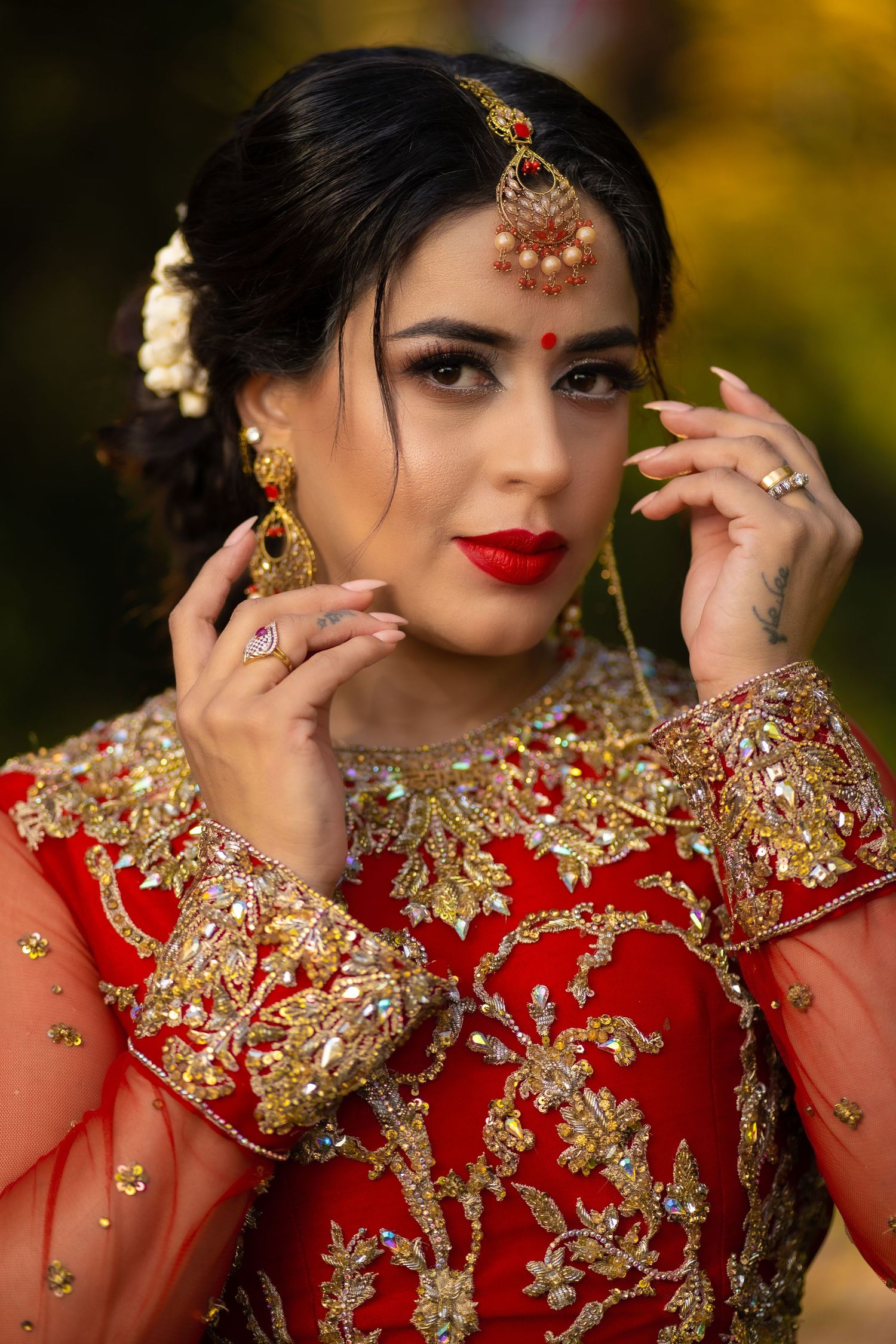 Traditional South Asian bridal attire featuring red and gold embroidered dress with ornate jewelry and accessories.