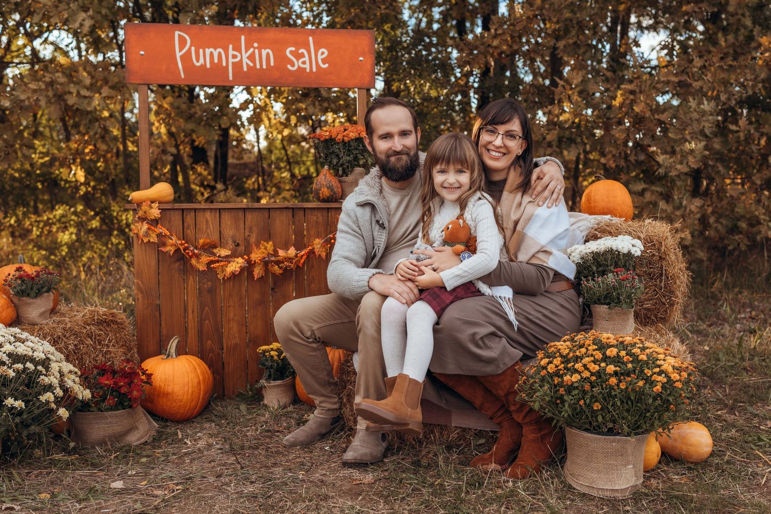 A cozy autumn scene with a rustic pumpkin sale display featuring orange pumpkins, mums and fall foliage.