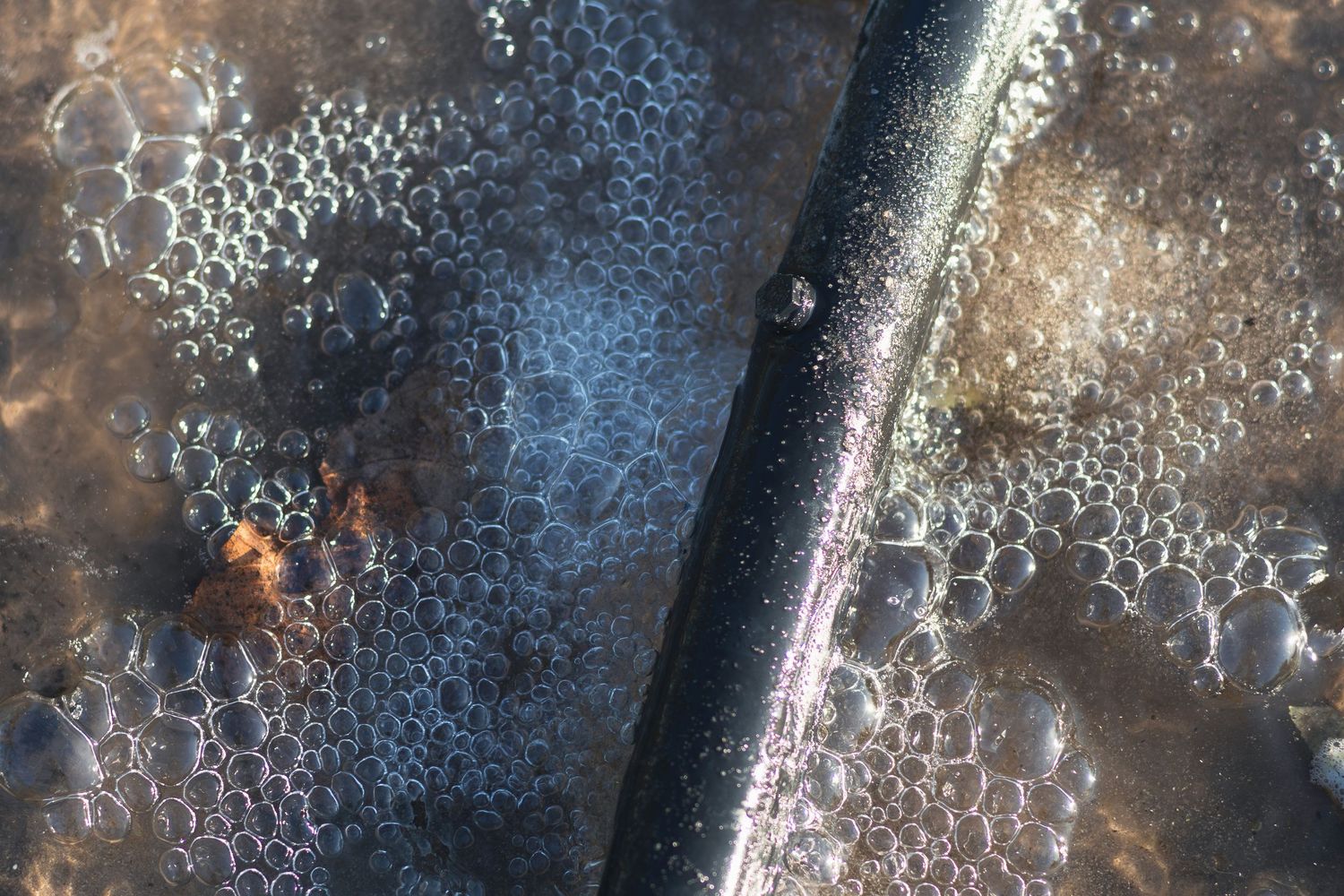 Close-up of a dark pipe surrounded by water bubbles and foam on a wet surface.