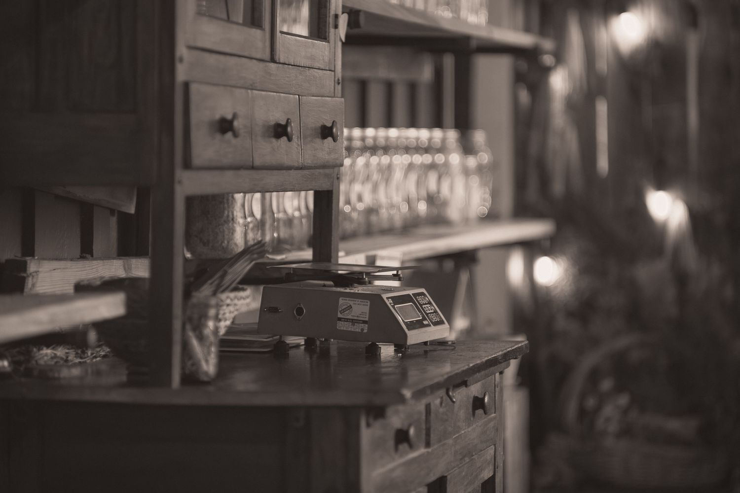 Vintage sepia-toned apothecary shop interior with antique wooden drawers, glass bottles on shelves, and an old weighing scale.