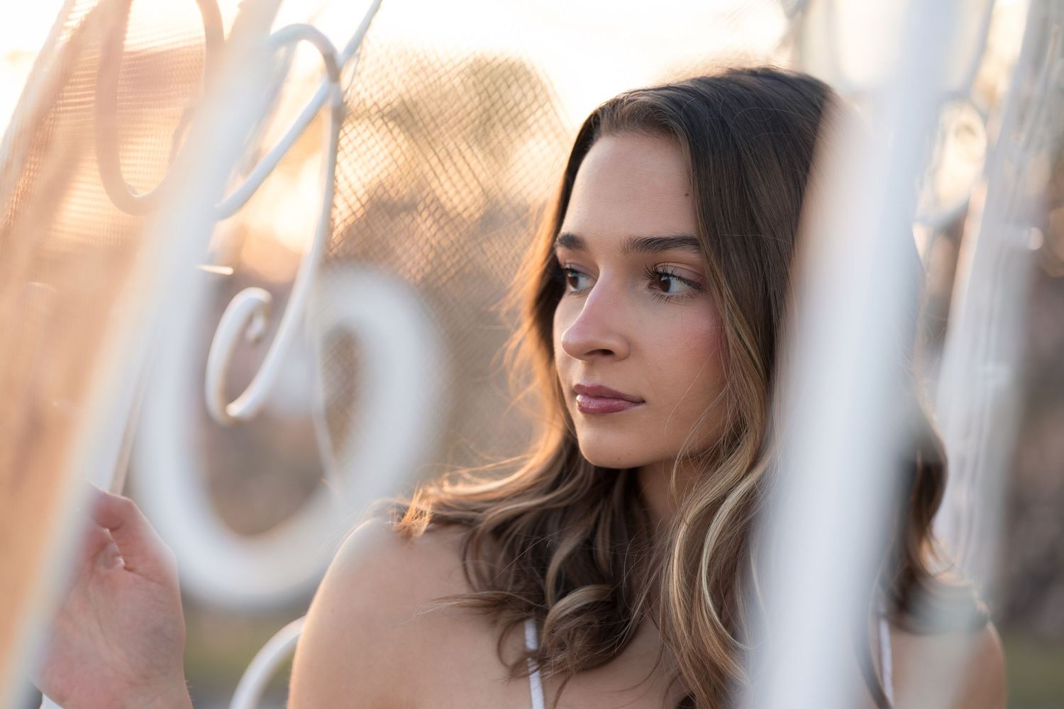 Woman with long brown hair looks thoughtfully into the distance with a soft glow of sunlight behind her.