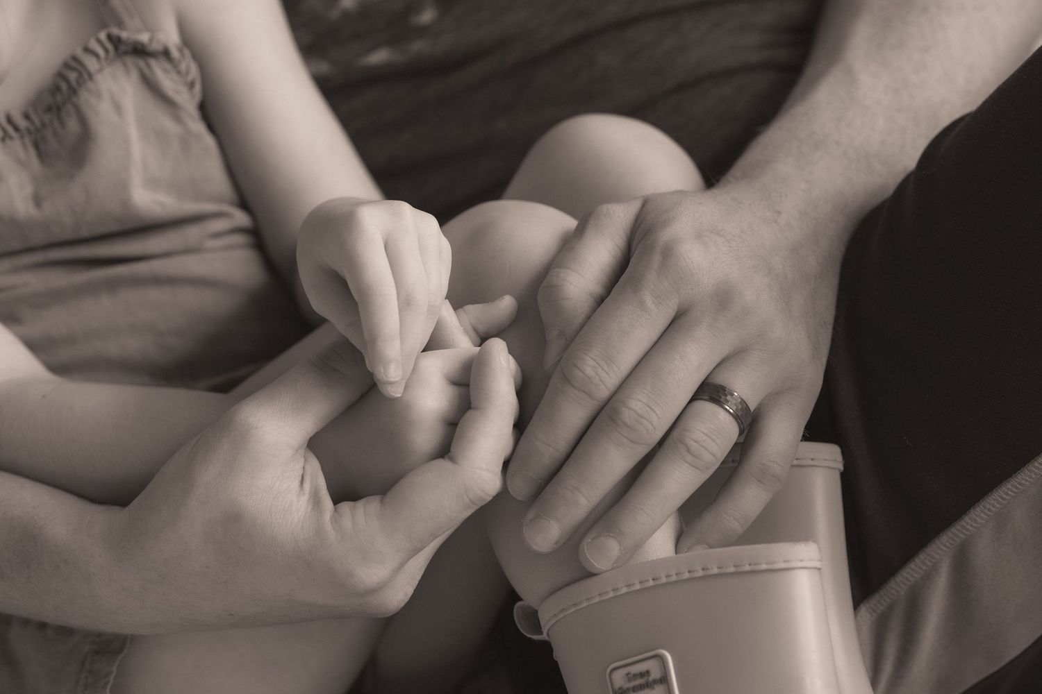 Black and white photo of adult hands gently holding a newborn baby's tiny hand, with a wedding ring visible.