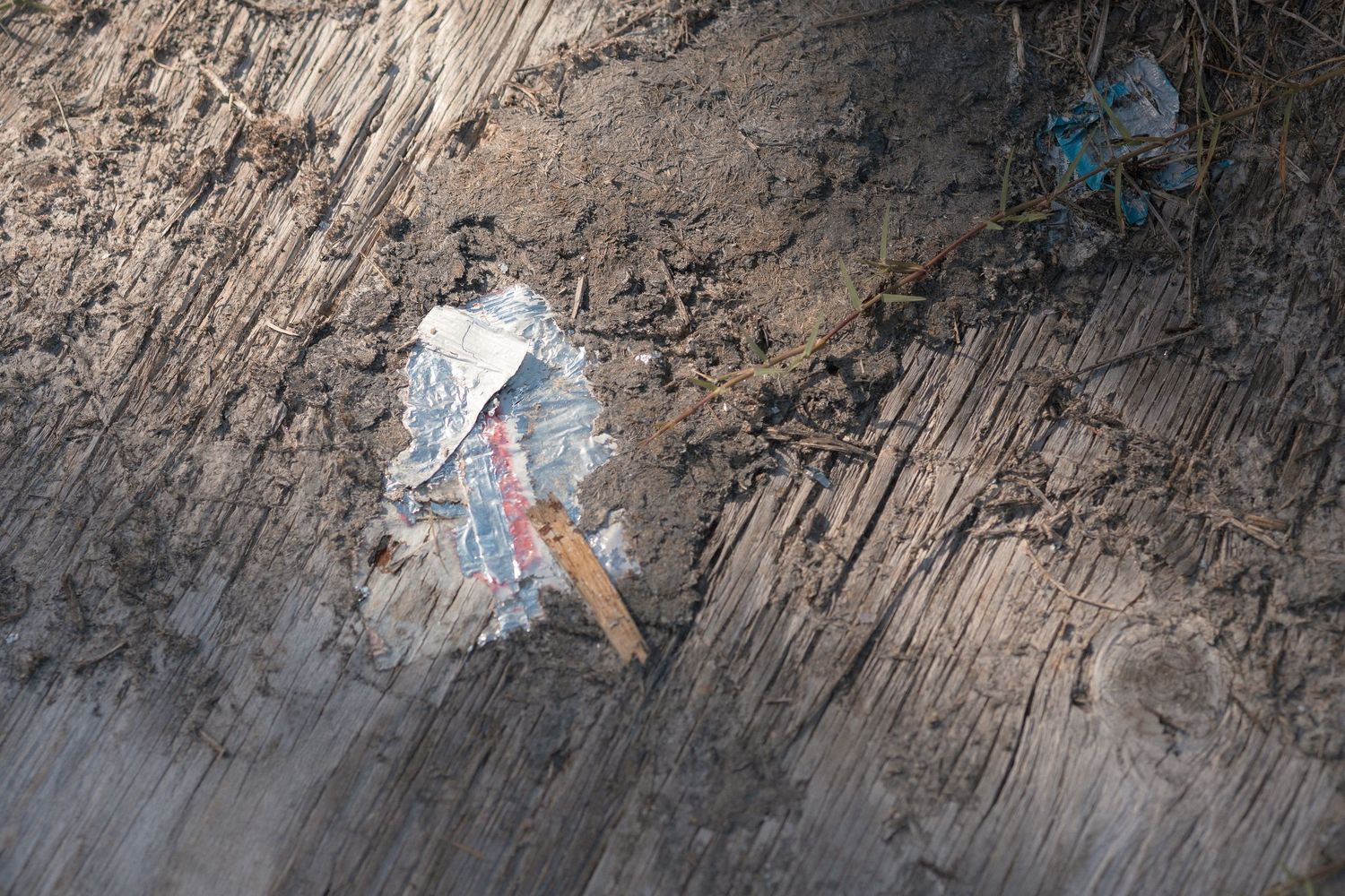 Close-up of torn paper and pencil embedded in layered muddy soil surface outdoors.