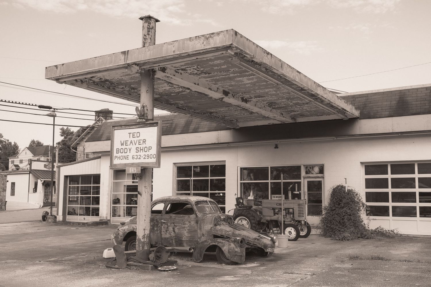 Vintage sepia photo of Ted Weaver Body Shop with rusty old trucks parked under a gas station canopy.