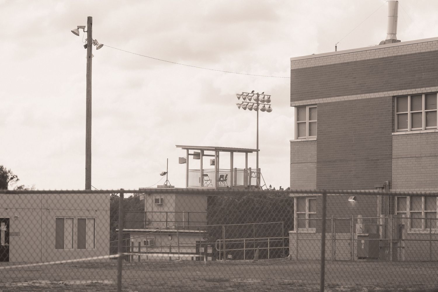 Sepia-toned photo of a fenced industrial facility with a brick building, utility pole, and elevated observation tower.
